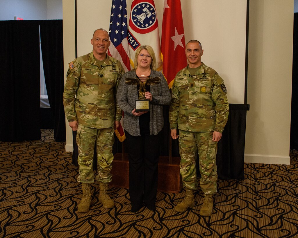 two men wearing u s army uniforms pose for a photo with a woman holding an award.