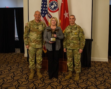 two men wearing u s army uniforms pose for a photo with a woman holding an award.