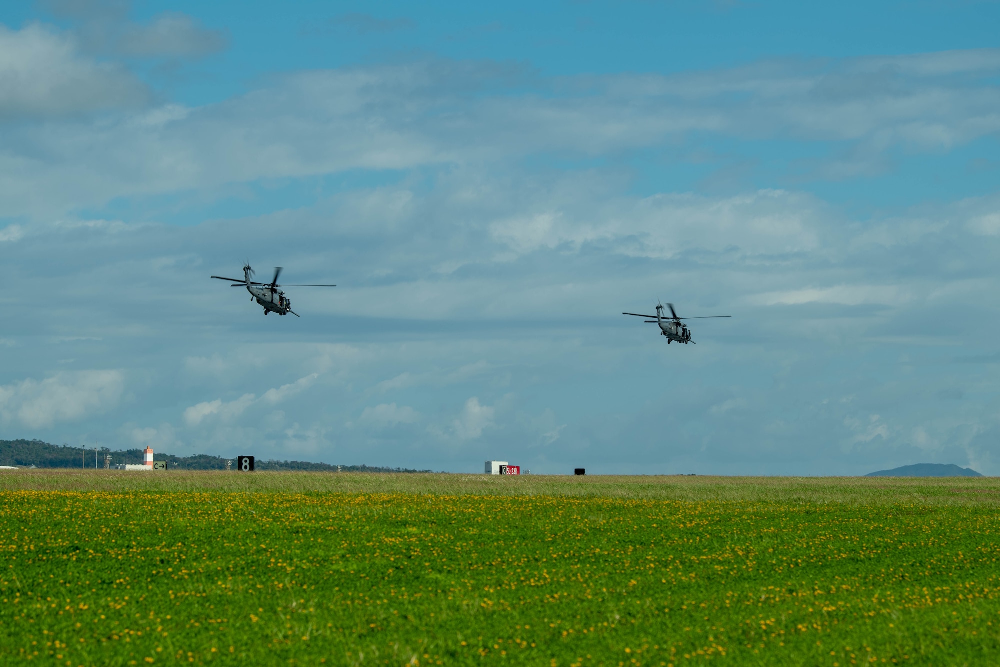 Two helicopters fly over runway.