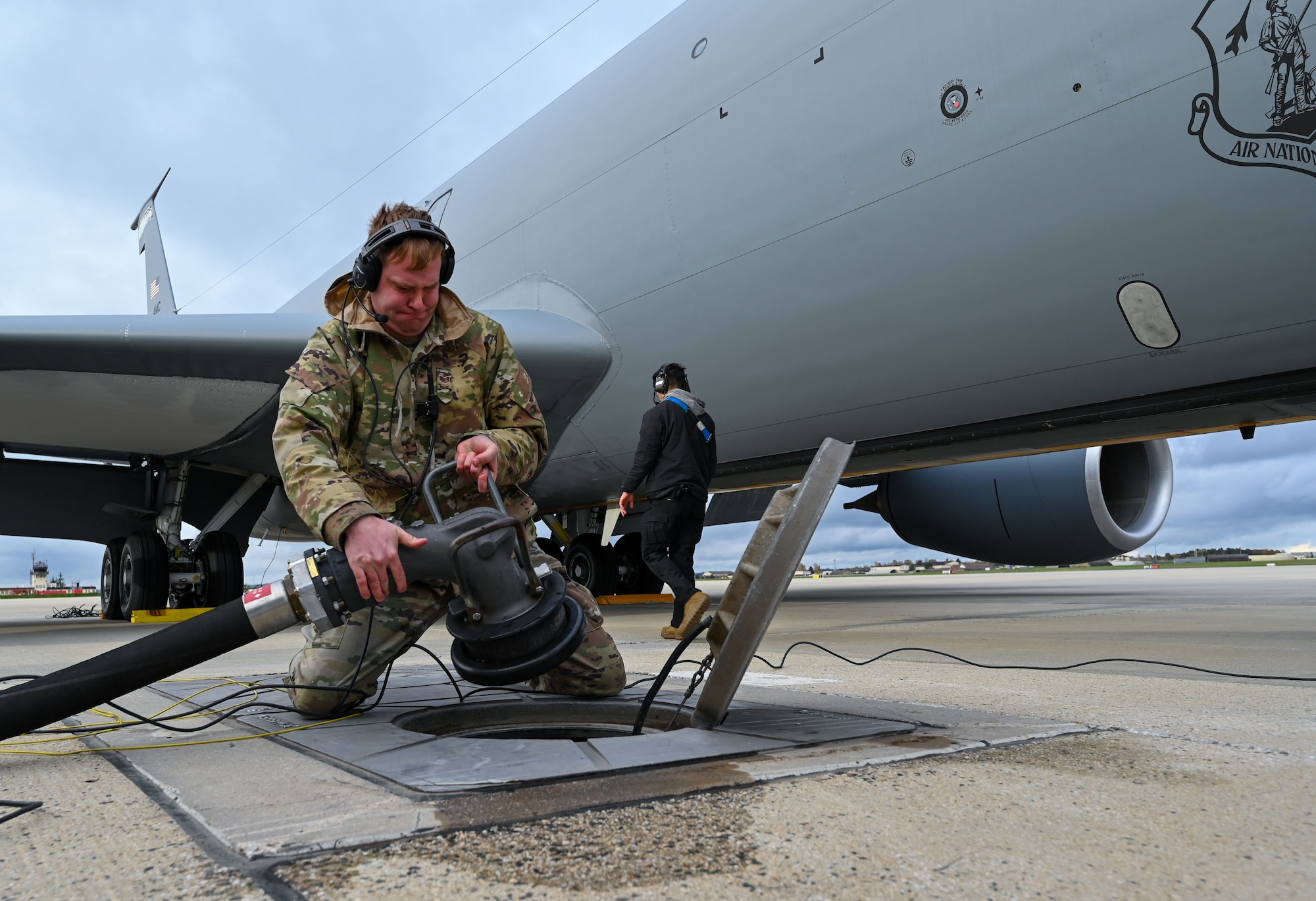 An Airman connects a hose to an underground fuel pit.
