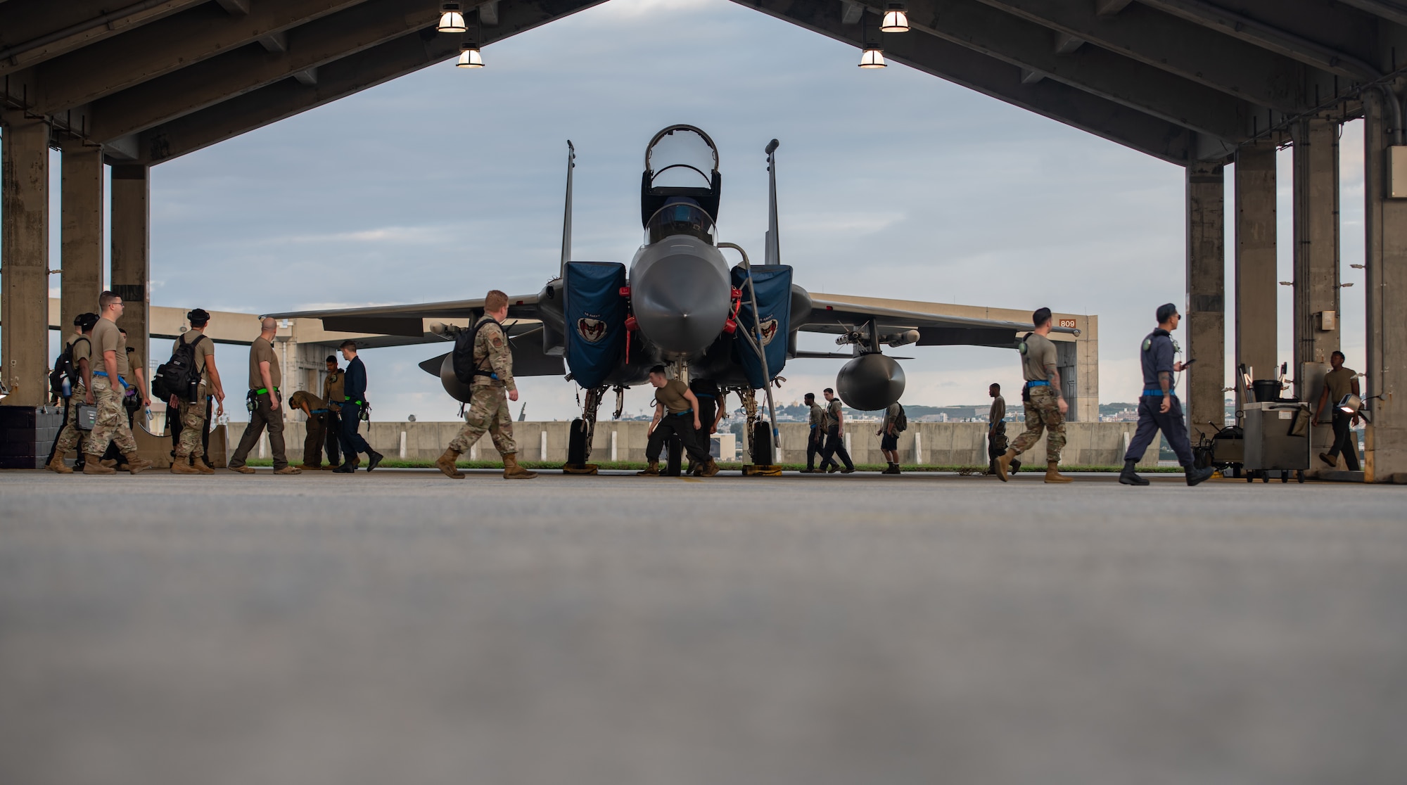Several Airmen walk around, in front and behind an F-15 Eagle.