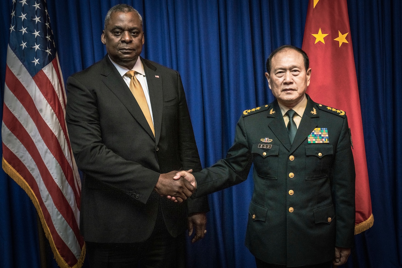 A man dressed in a business suit shakes hands with a man in a military uniform.