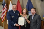 Air Force Col. Adrian Crowley, DLA Troop Support chief strategy officer, presents a certificate of retirement to Ngoc Phung Thi Le, an embroiderer in the DLA Troop Support Flag Room, as her husband, Trieu Thanh Dang, watches, during a ceremony Nov. 21, 2022 in Philadelphia. Le retired from the Flag Room after 14 years of service.