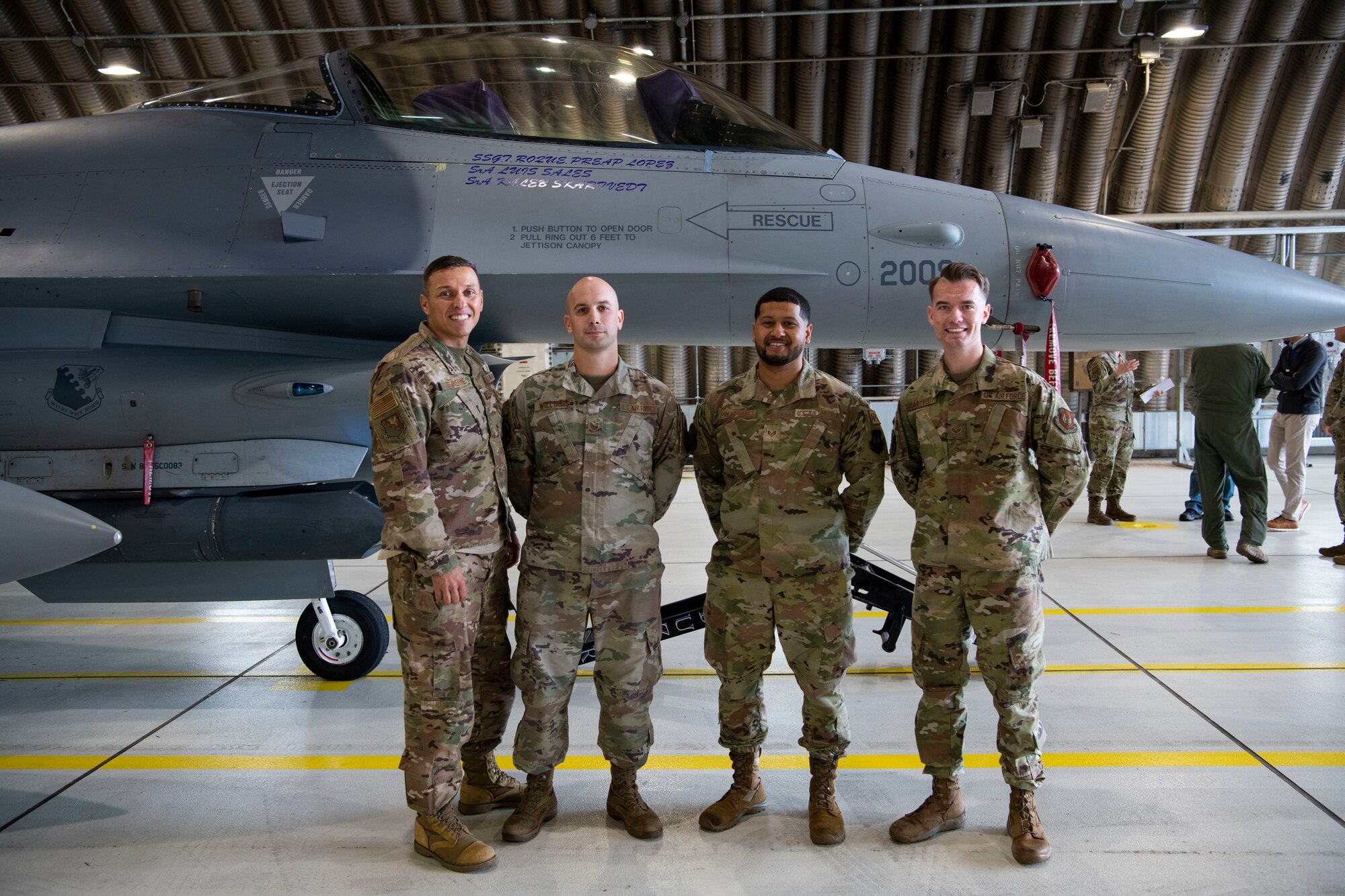Capt. Jerry St. Pierre, 31st Fighter Wing chaplain, left, coined Tech. Sgt. Jonathan Williams, 510th Fighter Generation Squadron avionics systems technician, left-middle, U.S. Air Force Staff Sgt. Roque Preap-Lopez, 510th FGS F-16 Fighting Falcon dedicated crew chief, right-middle, and Senior Airman Kaleb Skartvedt, 510th FGS F-16 Fighting Falcon assistant dedicated crew chief, right, at Aviano Air Base, Italy, Nov. 18, 2022. The three Airmen gave an F-16 electronic and mechanical systems briefing to Chaplain (Maj. Gen.) Randall Kitchens, U.S. Air Force chief of chaplains, and Chief Master Sgt. Sadie Chambers, U.S. Air Force religious affairs career field manager. (U.S. Air Force photo by Airman 1st Class Thomas Calopedis)