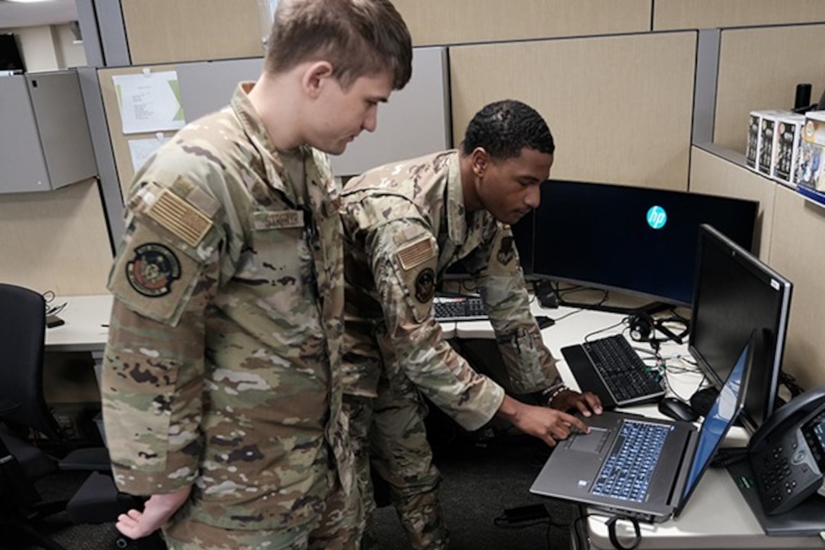 two military members stand working on computer