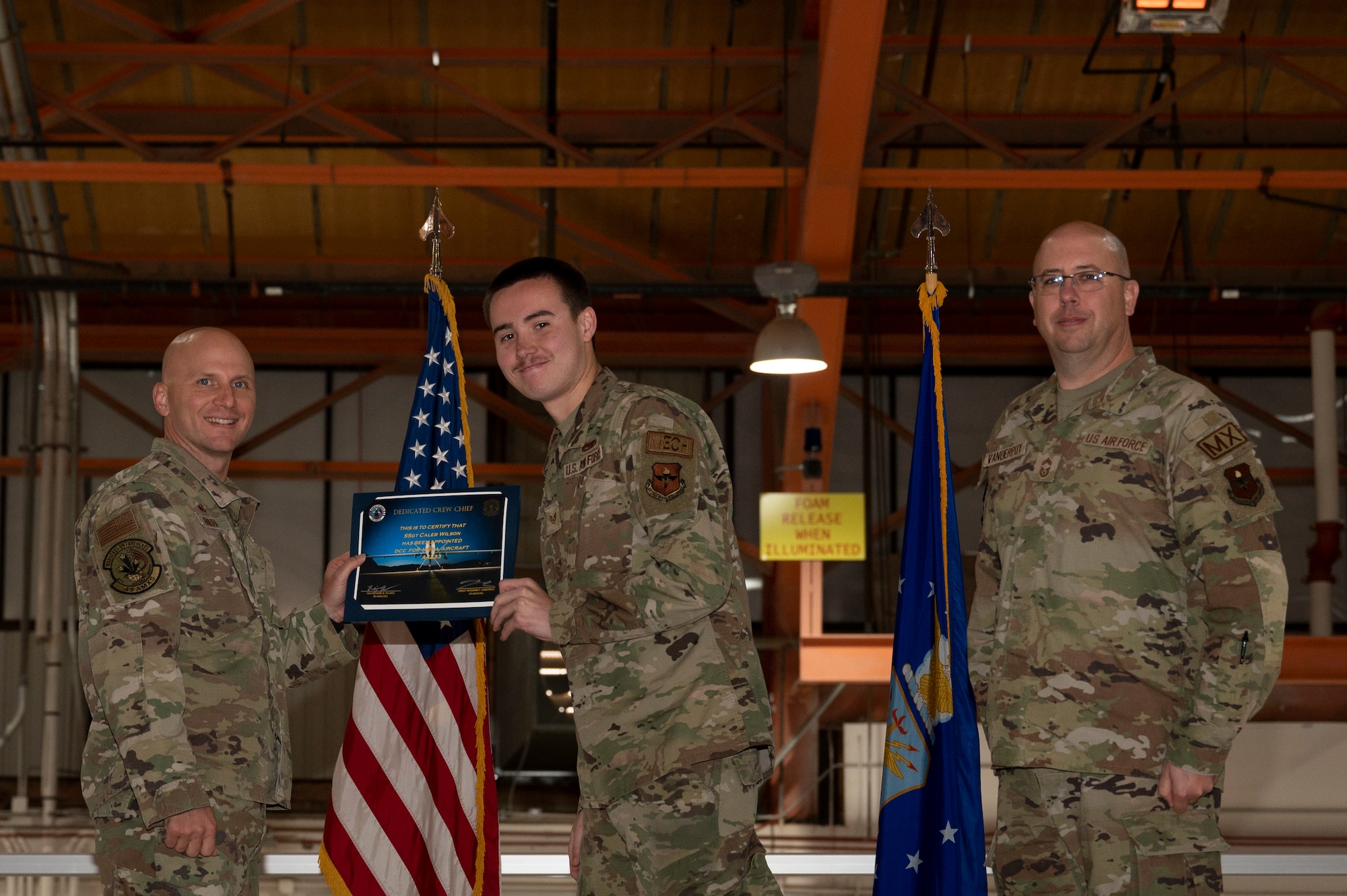 U.S. Air Force Staff Sgt. Caleb Wilson, 49th Aircraft Maintenance Squadron crew chief, center, receives a certificate from U.S. Air Force Maj. Donald Bolda, 49th Aircraft Maintenance Squadron commander, left, during the 2022 Dedicated Crew Chief Appointment Ceremony at Holloman Air Force Base, New Mexico, Nov. 18, 2022. To receive the title of DCC, a crew chief must demonstrate a history of superior performance in their career, comply with all safety practices and complete all required training. (U.S. Air Force photo by Airman 1st Class Isaiah Pedrazzini)