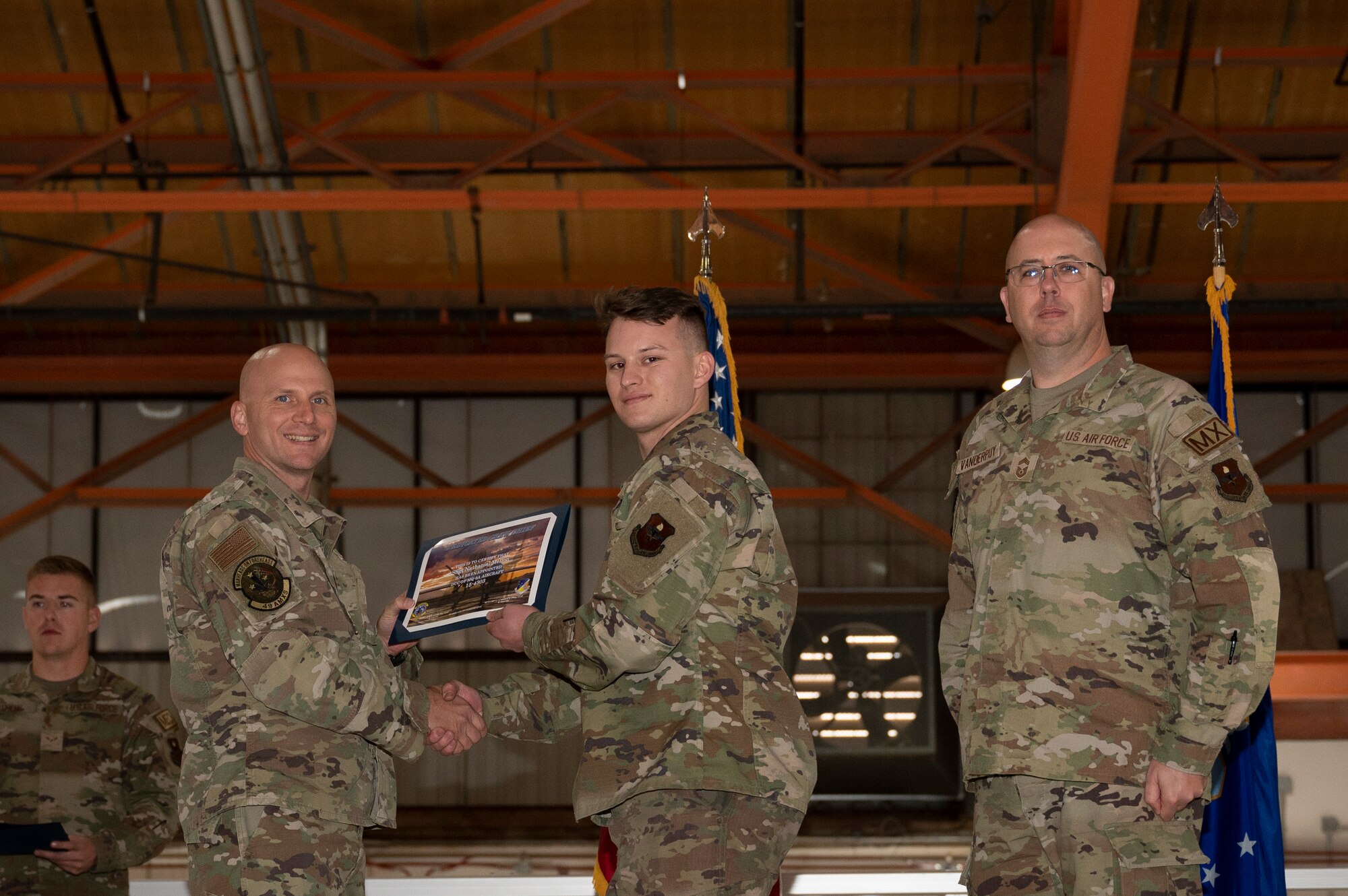 U.S. Air Force Staff Sgt. Nathanial Mellon, 49th Aircraft Maintenance Squadron crew chief, center, receives a certificate from U.S. Air Force Maj. Donald Bolda, 49th Aircraft Maintenance Squadron commander, left, during the 2022 Dedicated Crew Chief Appointment Ceremony at Holloman Air Force Base, New Mexico, Nov. 18, 2022. To receive the title of DCC, a crew chief must demonstrate a history of superior performance in their career, comply with all safety practices and complete all required training. (U.S. Air Force photo by Airman 1st Class Isaiah Pedrazzini)