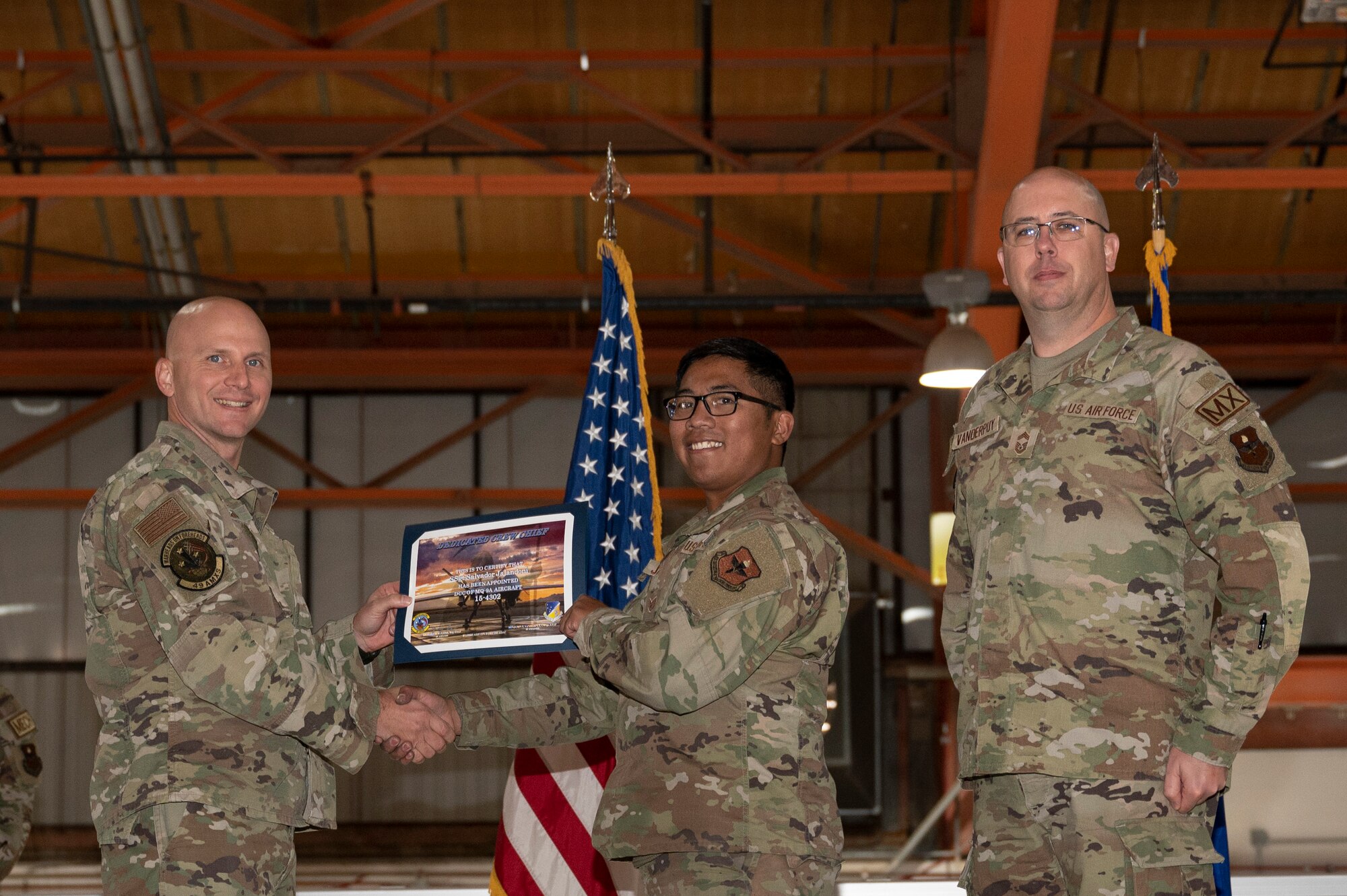 U.S. Air Force Staff Sgt. Salvador Jalandoni, center, 49th Aircraft Maintenance Squadron crew chief, receives a certificate from U.S. Air Force Maj. Donald Bolda, 49th Aircraft Maintenance Squadron commander, left, during the 2022 Dedicated Crew Chief Appointment Ceremony at Holloman Air Force Base, New Mexico, Nov. 18, 2022. To receive the title of DCC, a crew chief must demonstrate a history of superior performance in their career, comply with all safety practices and complete all required training. (U.S. Air Force photo by Airman 1st Class Isaiah Pedrazzini)