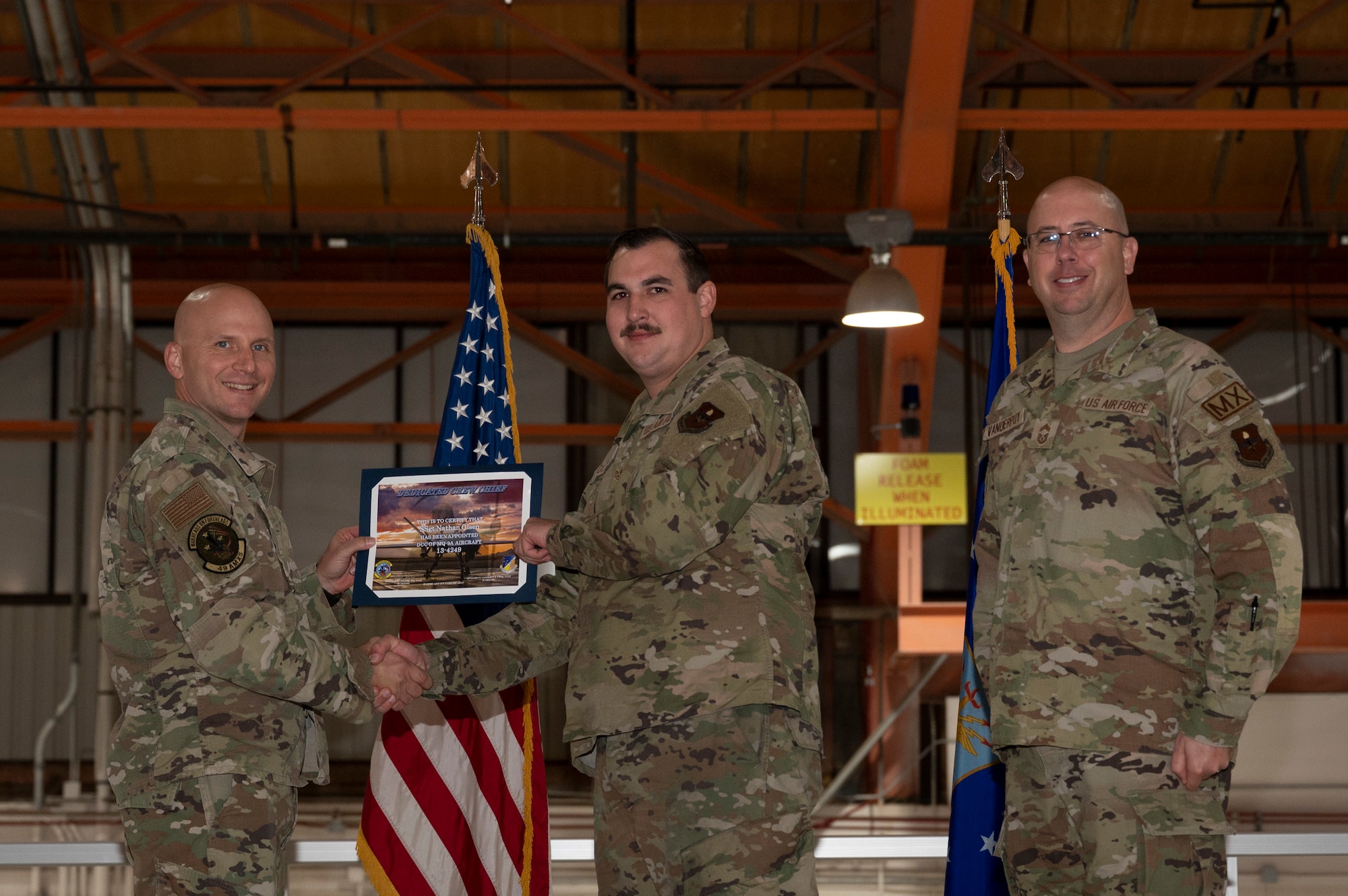 U.S. Air Force Staff Sgt. Nathan Olsen,
49th Aircraft Maintenance Squadron crew chief, center, receives a certificate from U.S. Air Force Maj. Donald Bolda, 49th Aircraft Maintenance Squadron commander, left, during the 2022 Dedicated Crew Chief Appointment Ceremony at Holloman Air Force Base, New Mexico, Nov. 18, 2022. To receive the title of DCC, a crew chief must demonstrate a history of superior performance in their career, comply with all safety practices and complete all required training. (U.S. Air Force photo by Airman 1st Class Isaiah Pedrazzini)