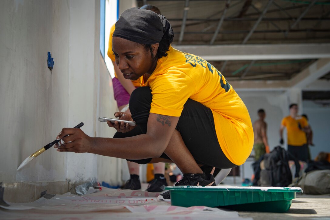 A sailor in civilian clothes kneels and paints a wall.