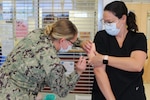 A phot of a female Navy corpsman practicing giving an immunization to a staff nurse.