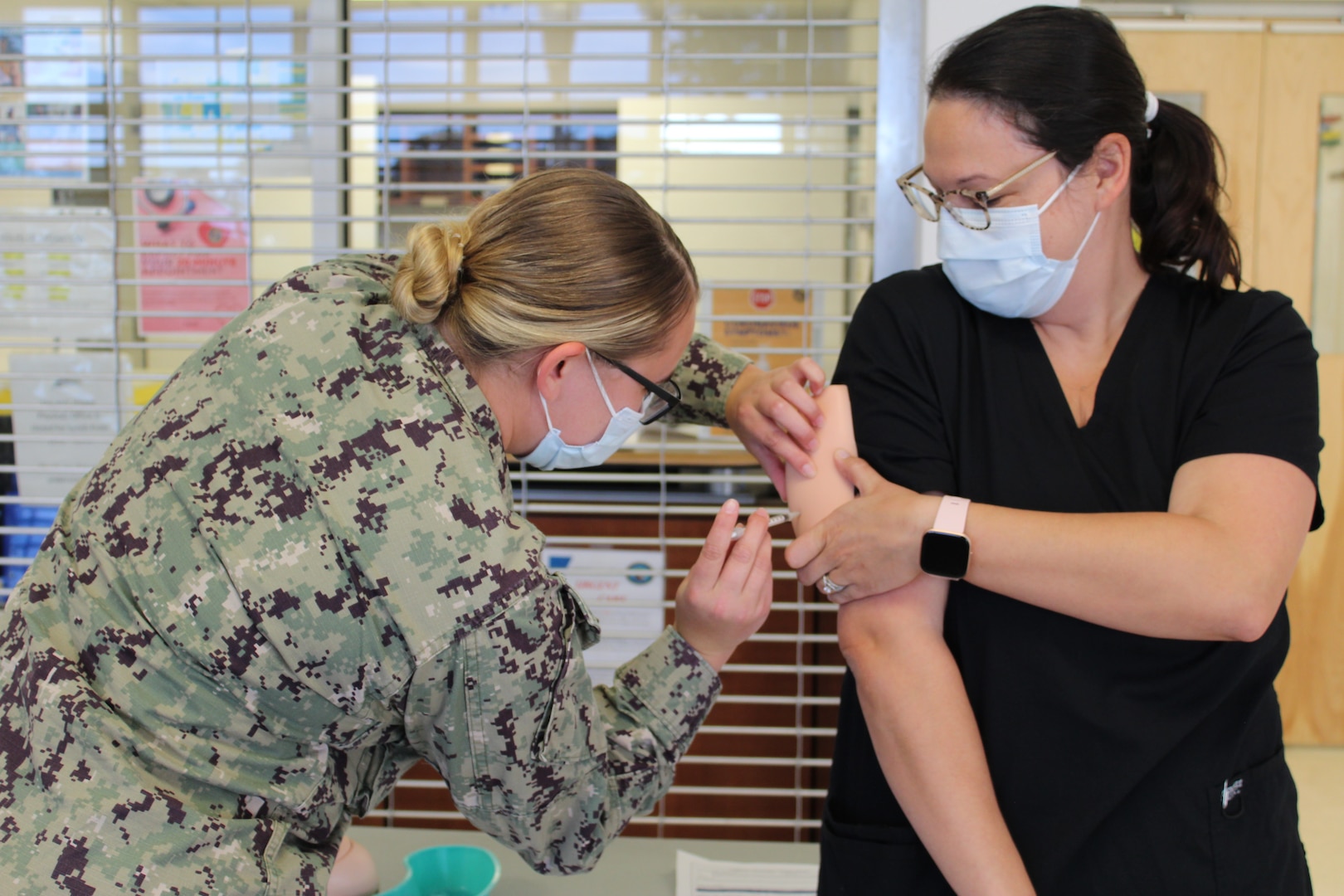 A phot of a female Navy corpsman practicing giving an immunization to a staff nurse.