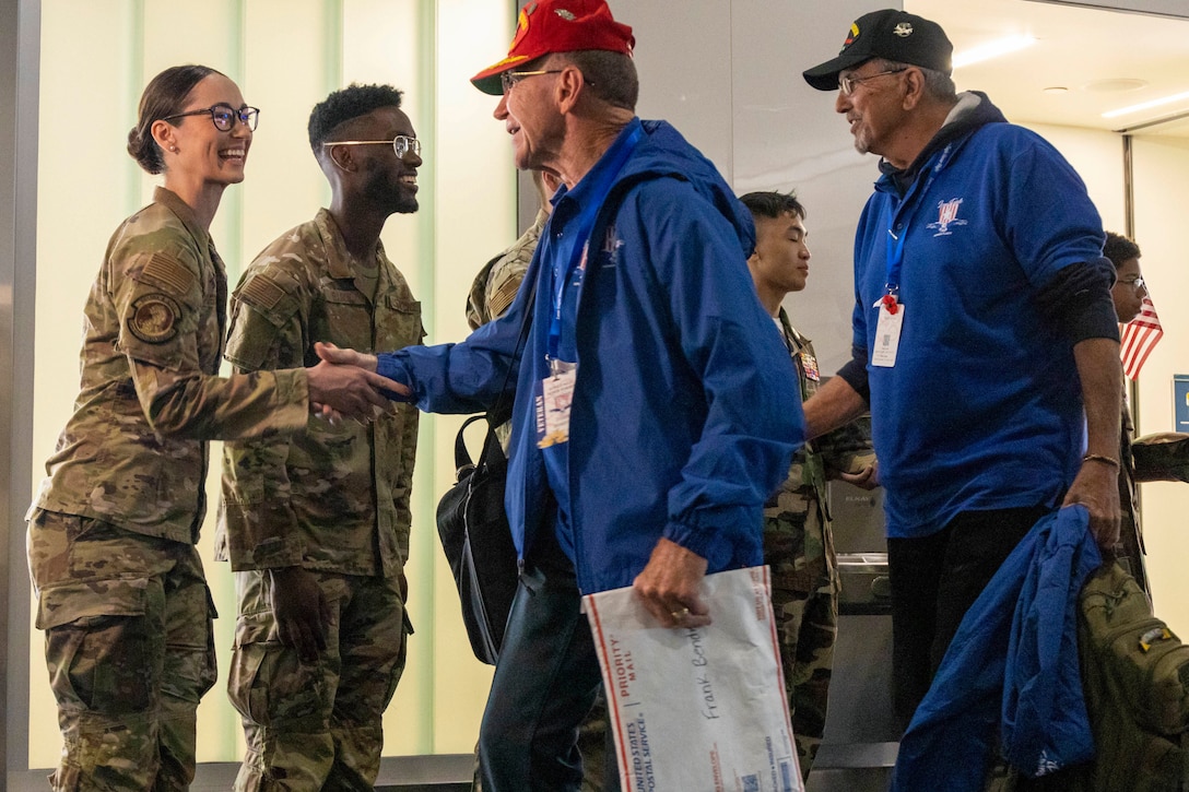 Airmen standing in a line smile and shake hands with veterans at an airport.