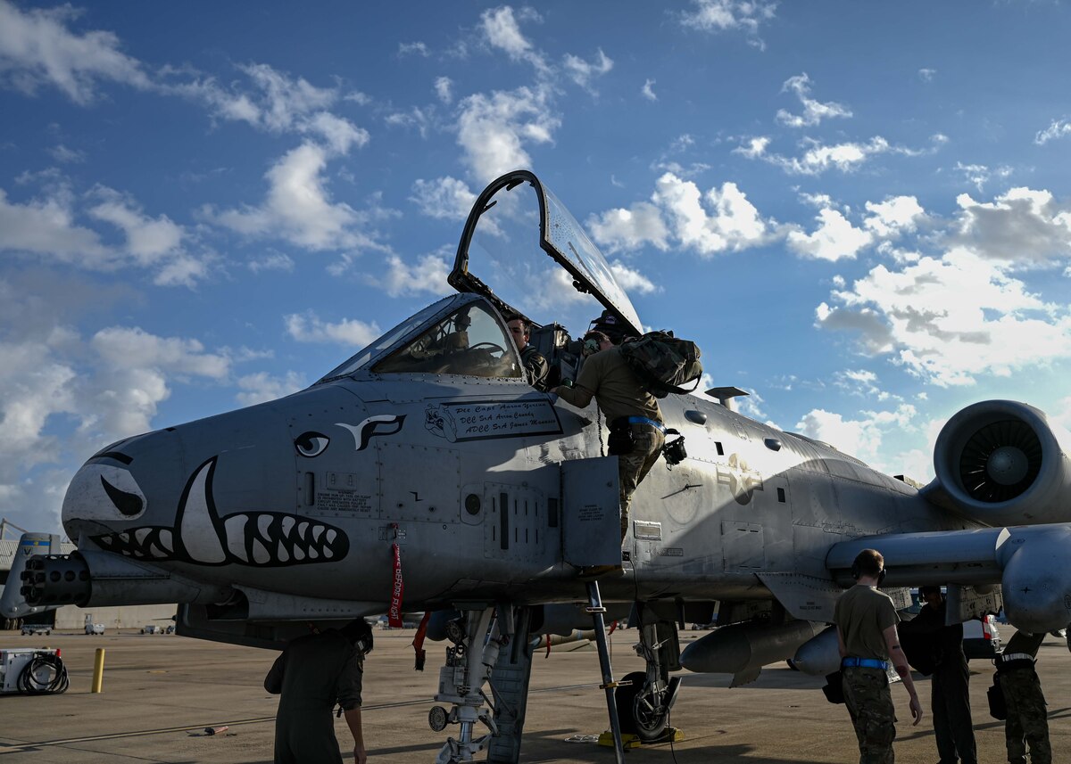 A photo of a man in a military uniform exiting a plane while other people in military uniforms work on the plane.