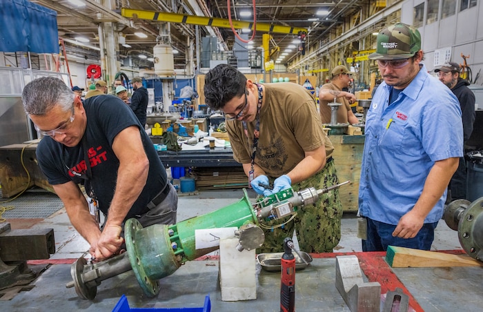 Dylan Whaley, an electrician's mate third class assigned to USS Theodore Roosevelt (CVN 71), center, gets help disassembling a valve from Erik Kendrickson, right, a technician from contracting partner Curtiss Wright Fleet Solutions and John Devito, left, a technician from contracting partner Target Rock. (U.S. Navy photo by Wendy Hallmark)