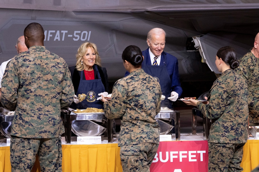 The president and first lady, wearing aprons, serve food at a buffet table to service members.