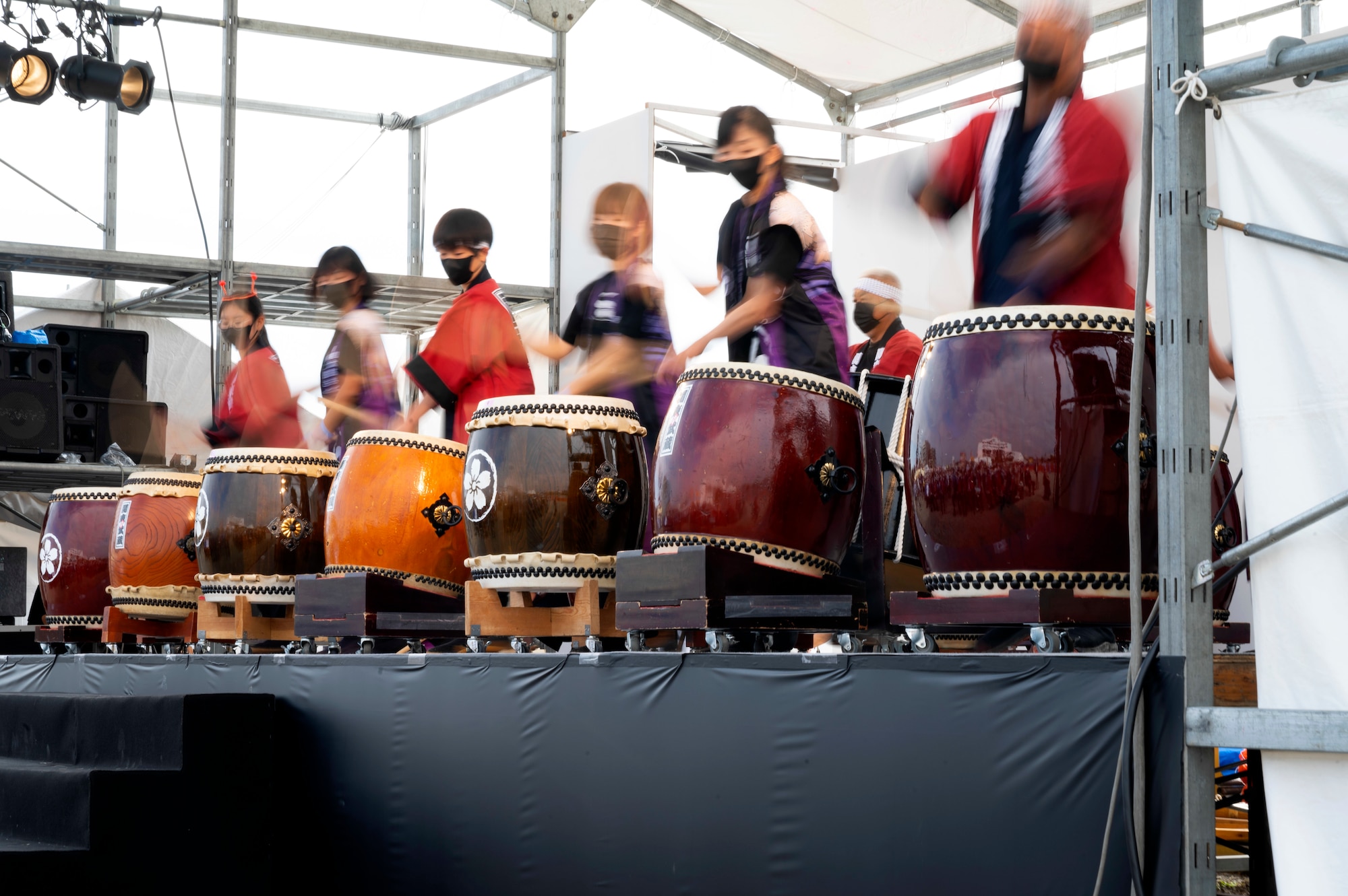 Taiko troupe plays large drums made out of barrels or tree trunks with cowhide covers to a crowd of Deedara Festival attendee. The musicians beat the drums in unison to produce loud, reverberating beats
