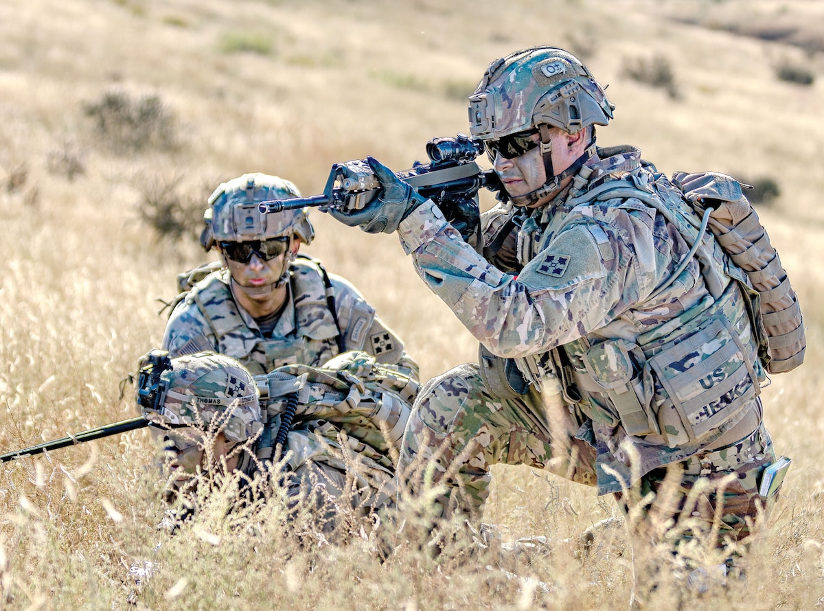 three military members in a field, one holding a rifle