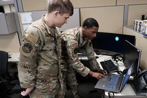two military members stand working on computer