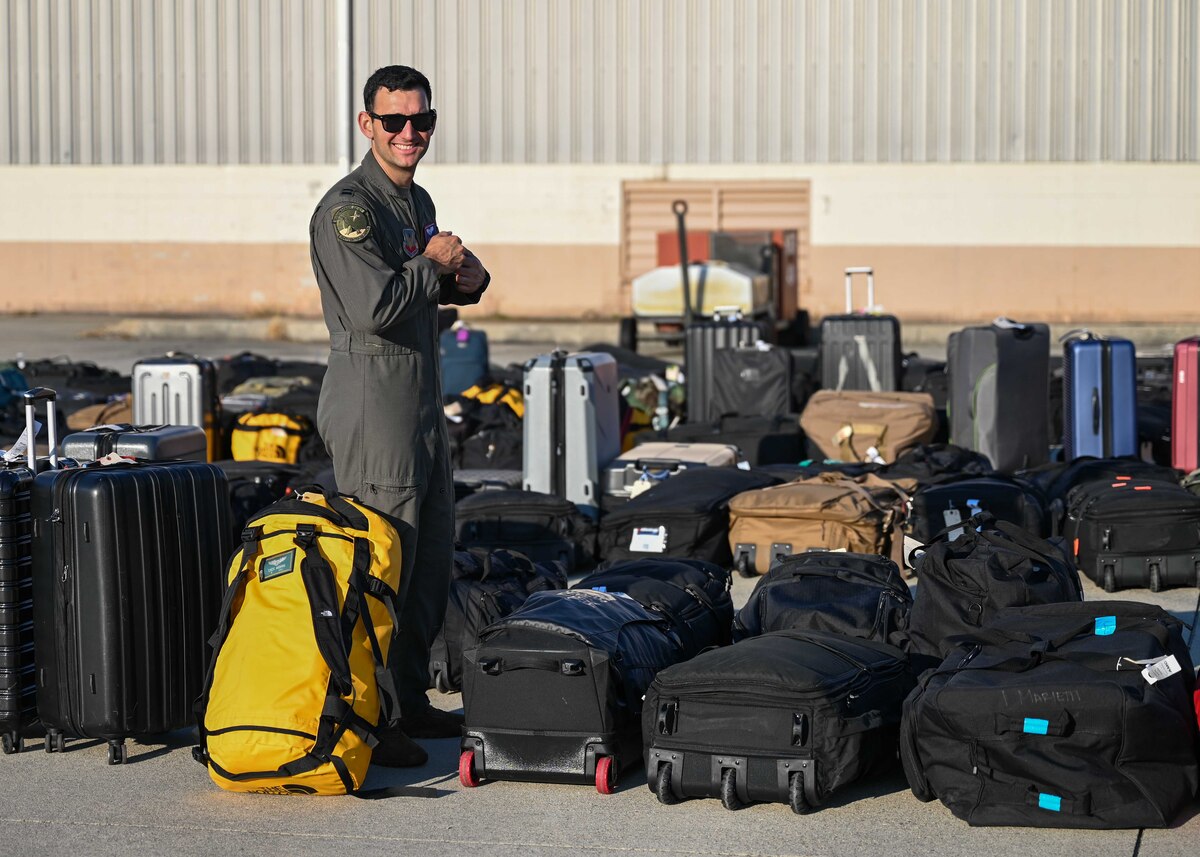 A photo of a man in a military uniform searches through rows of bags to find his.
