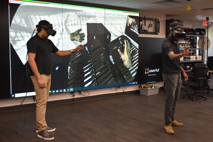 IMAGE: – NSWCDD Computer Scientists Amit Nemani and Brandon Gipson show the 30mm virtual gun trainer, an application of the Battle Management System in the virtual realm. The trainer is not designed to replace hands-on training but allow operators easier accessibility to the system.