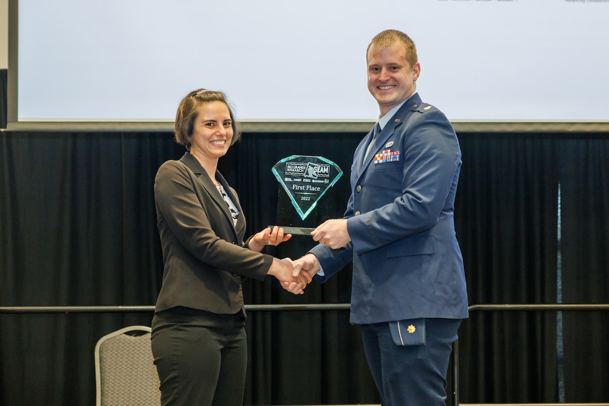 Maj. Joshua Reding of the Air Force Research Laboratory, or AFRL, Directed Energy Directorate presents Tessily Hogancamp, a chemist from Sandia National Laboratories, or SNL, a trophy as the first-place winner of the Rio Grande Research SLAM, a postdoctoral speech competition in Albuquerque, New Mexico, Nov. 5, 2022. Reding, who stepped in at the last minute as the master of ceremonies and whom the organizers called “amazing,” presided over the event that included postdoctoral researchers from AFRL, SNL, Los Alamos National Lab and the New Mexico Established Program to Stimulate Competitive Research. (Courtesy photo)