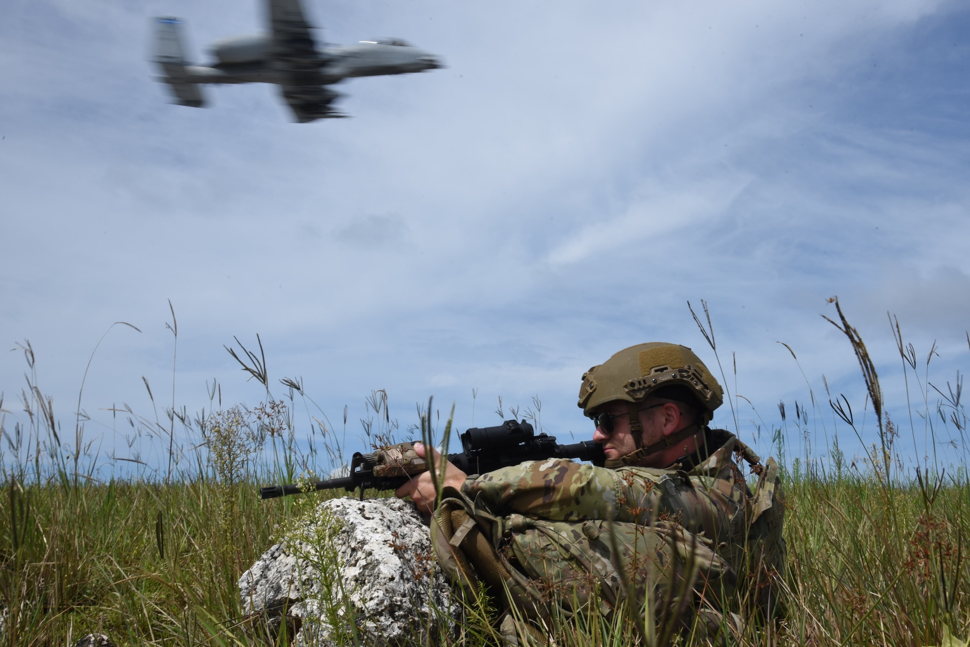 Photo of an Airman kneeling in a field near a runway