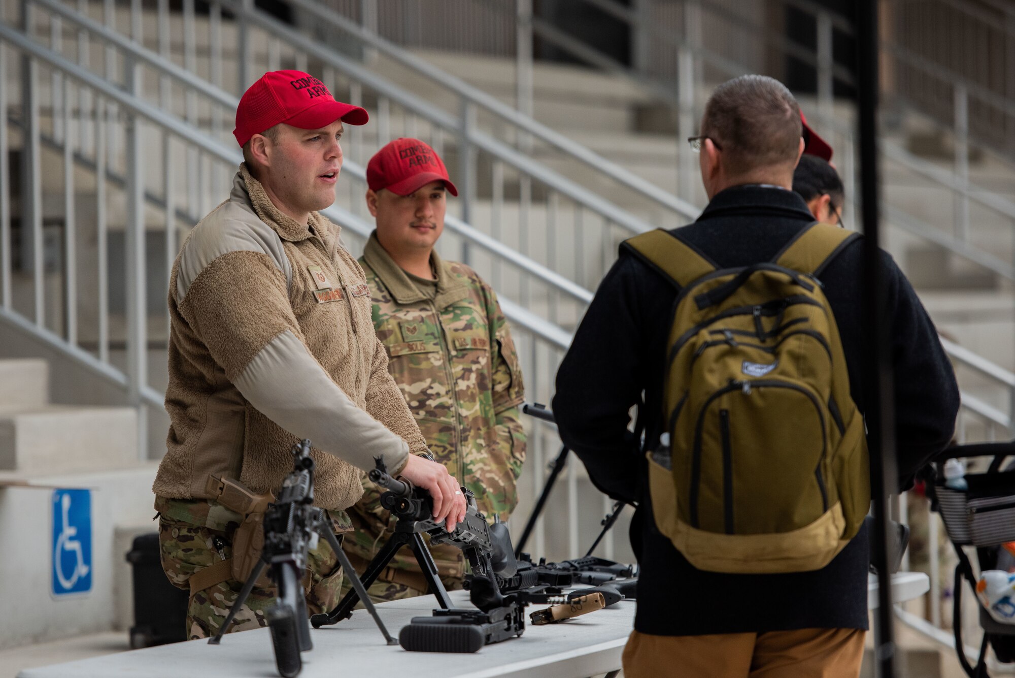 Two men are speaking about the military weapons displayed on a table