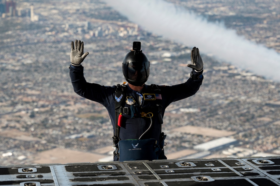 A airman puts their hands up after jumping from the open doorway of an airborne aircraft.