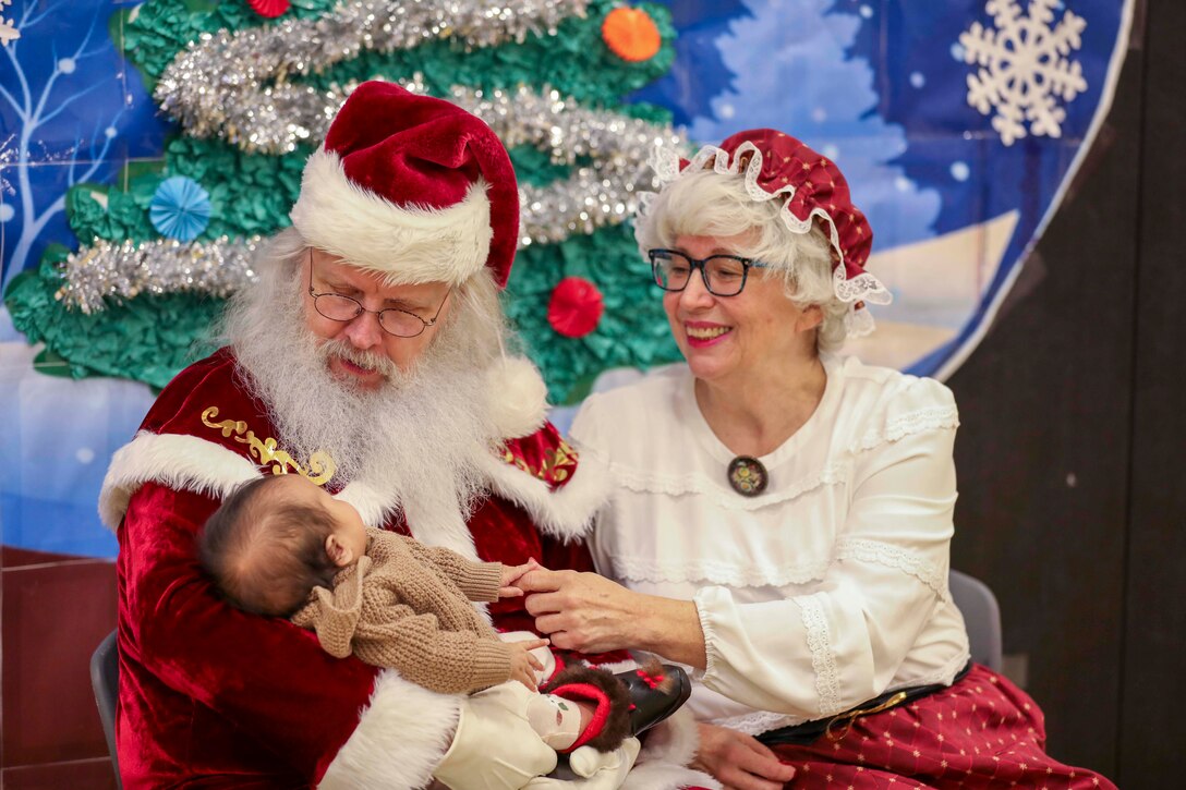 Santa and Mrs. Claus are seen smiling as he holds a baby.