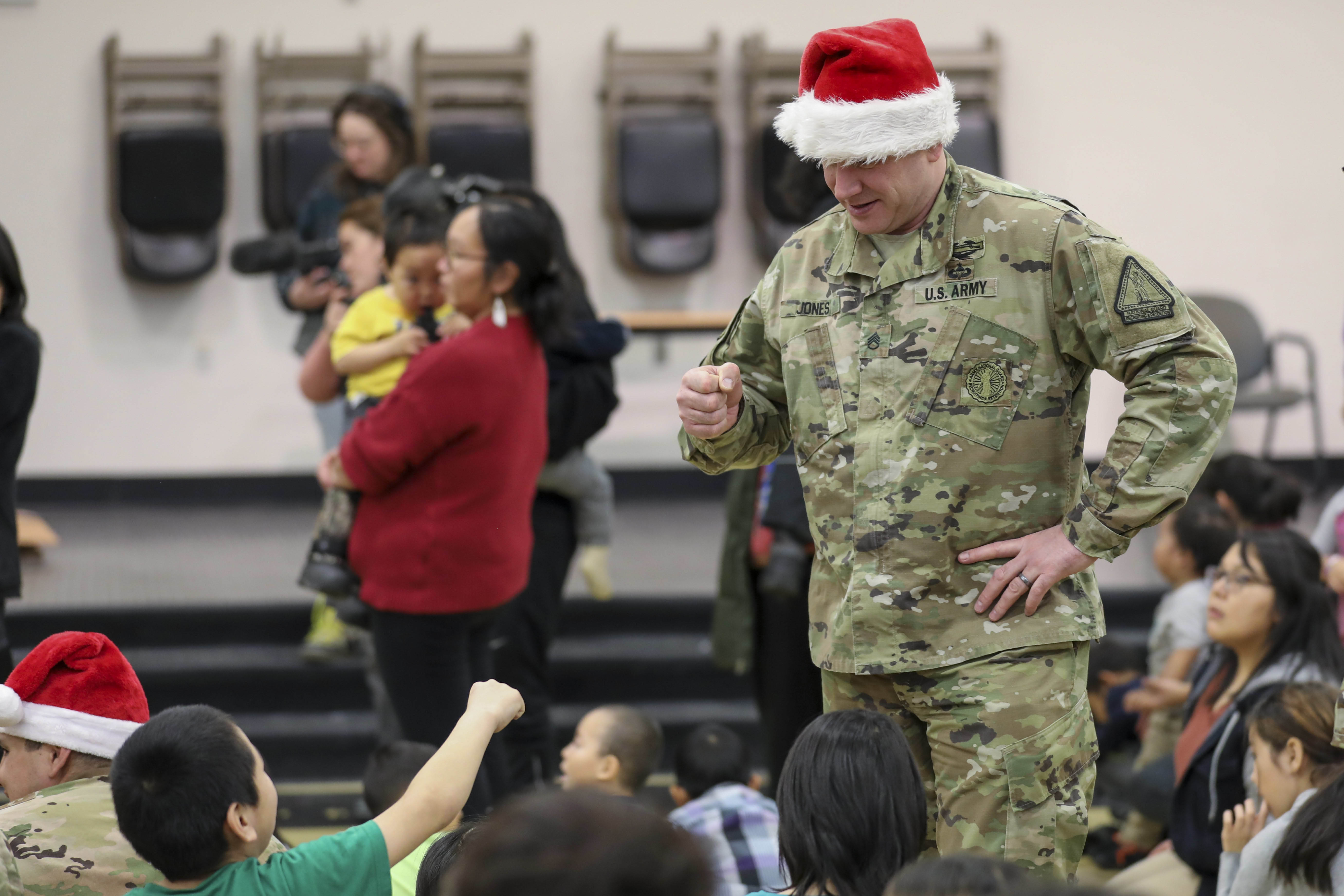 A soldier wearing a santa hat talks to a group of children