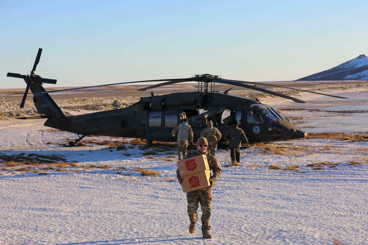 Soldier in uniform is seen carrying boxes away from a helicopter.