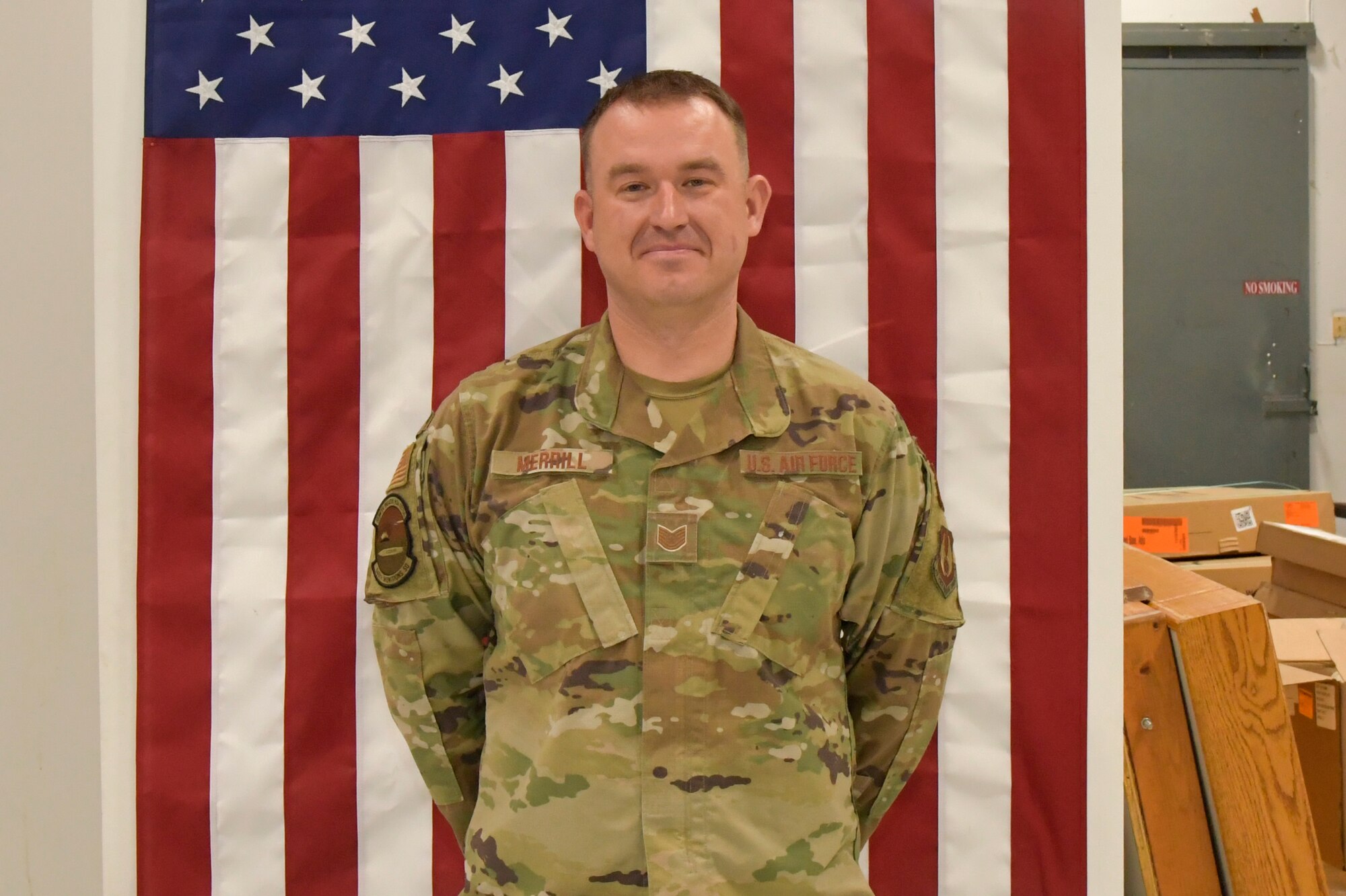 Technical Sgt. Alexander Merrill, 649th Munitions Squadron, stands at parade rest wearing his new rank in front of an American flag draped on the wall.