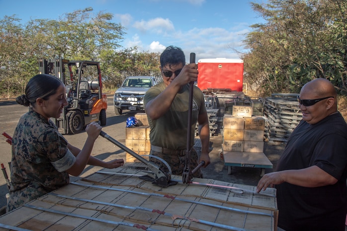 U.S. Marines and a civilian with Headquarters Battalion, Ammunition Supply Point, clamp metal straps and secure ammunition crates to pallets, Marine Corps Base Hawaii, Nov. 17, 2022. Various units on MCBH, including the 13th Marine Expeditionary Unit, were supplied ammunition to support training exercises and ranges. (U.S. Marine Corps photo by Lance Cpl. Terry Stennett III)