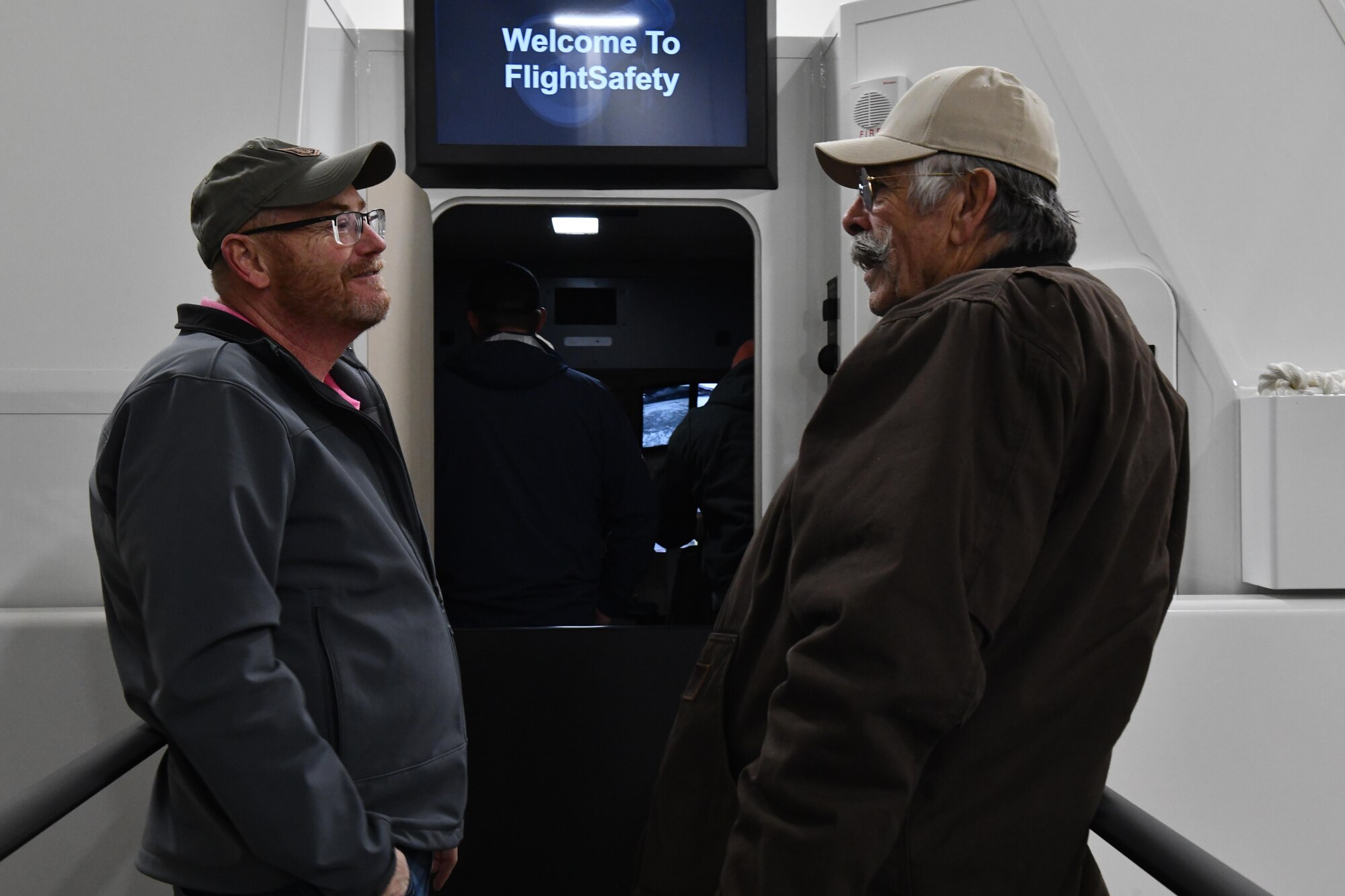 Steven Grice, 97th Training Squadron KC-46 contracting officer representative, speaks to Gary Winsett, Vietnam veteran, former pilot and local wheat farmer, outside of a KC-46 simulator at Altus Air Force Base, Oklahoma, Nov. 14, 2022. The simulators are crafted with a hydraulic system to ensure all movement is similar to what one would experience on a real flight. (U.S. Air Force photo by Airman 1st Class Miyah Gray)