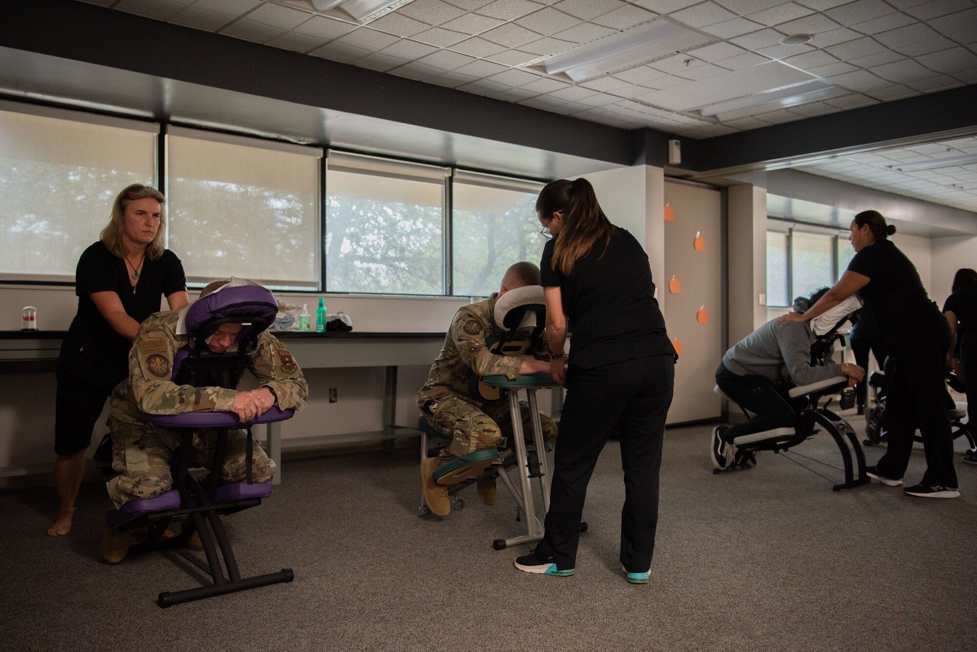 Men in military uniform sitting down on a massage chair while a massage therapist is massaging them