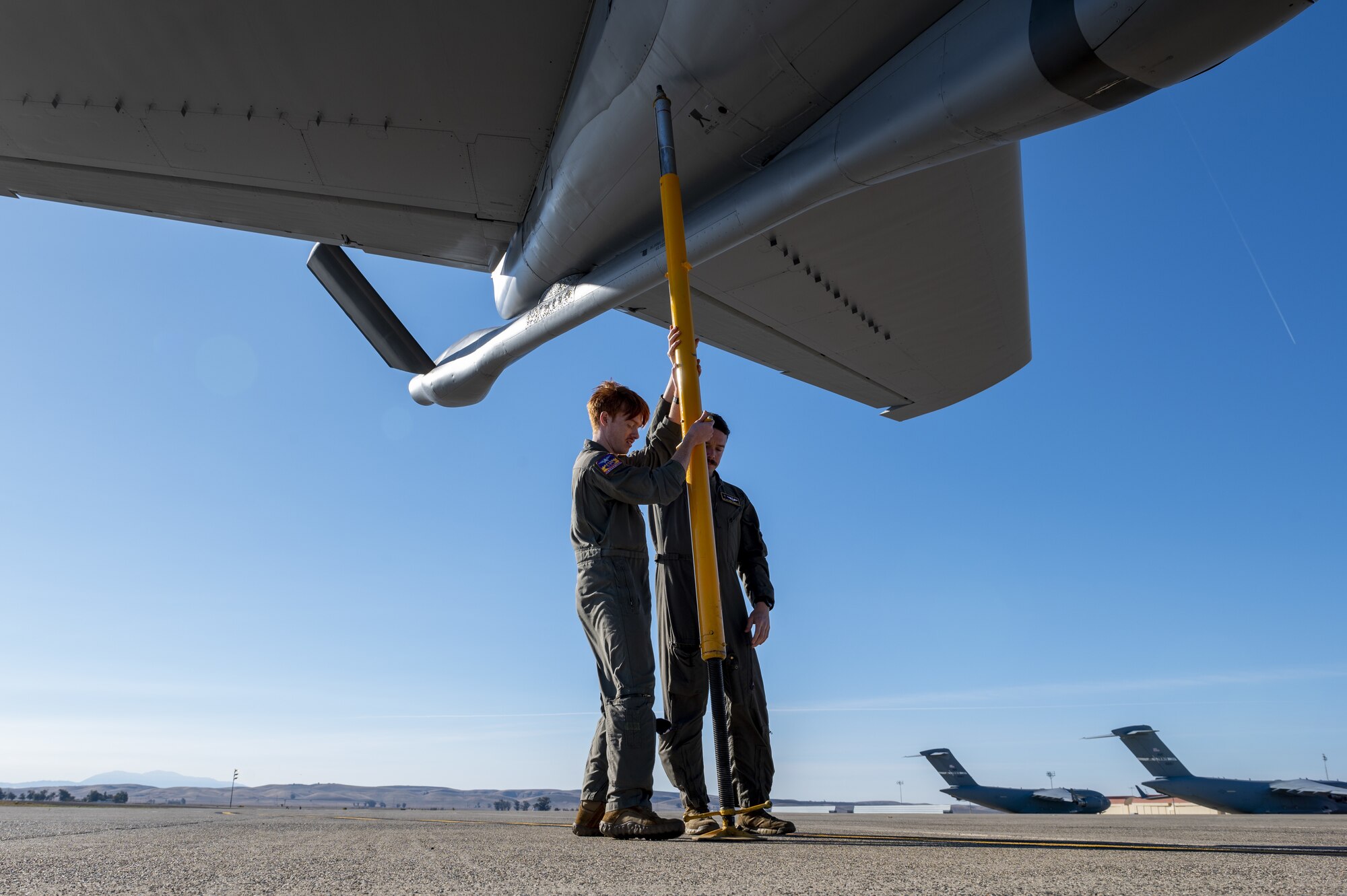 U.S. Air Force Senior Airman Matthew Ronnfeldt, 97th Air Refueling Squadron in-flight refueling specialist, and Senior Airman Dakota Griffis, 384th ARS in-flight refueling specialist, install a tail stand prior to receiving cargo on a KC-135 Stratotanker aircraft at Travis Air Force Base, California, Nov. 19, 2022. The mission required the crew to fly to Travis AFB where they loaded 8,000 pounds of cargo and supplies, followed by providing air refueling training for a C-17 Globemaster III aircraft from JBPHH. (U.S. Air Force photo by Staff Sgt. Lawrence Sena)