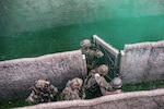 A soldier opens a fence door surrounded by green smoke as fellow soldiers follow.