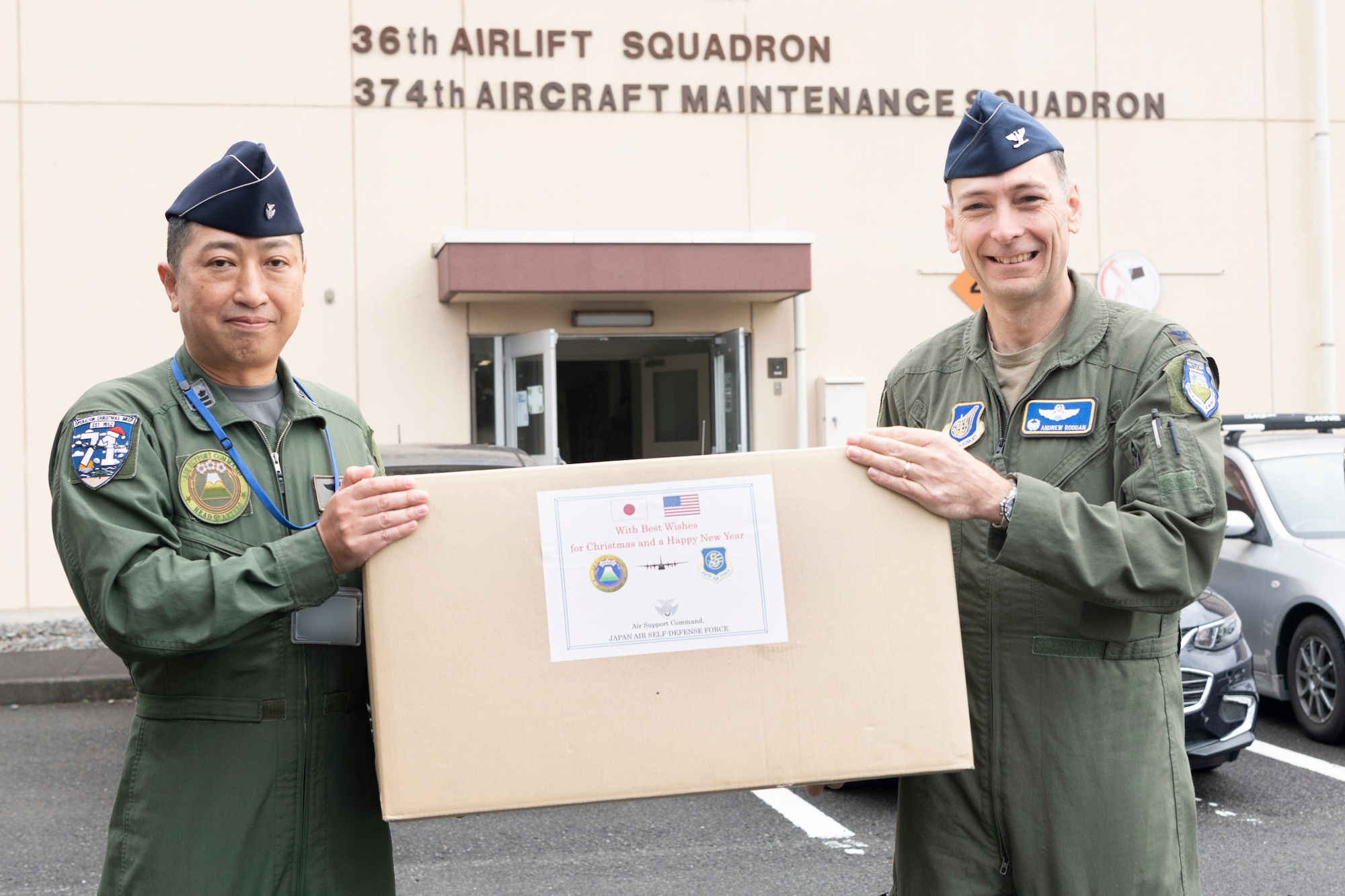 Col. Andrew Roddan, 374th Airlift Wing commander, accepts a donation of humanitarian supplies from Japan Air Self-Defense Force Lt. Col. Takahiro Seki, Headquarters Air Support Command, A3/5 Directorate, A5 Division senior officer, in preparation for Operation Christmas Drop at Yokota Air Base, Japan, Nov. 21, 2022.
