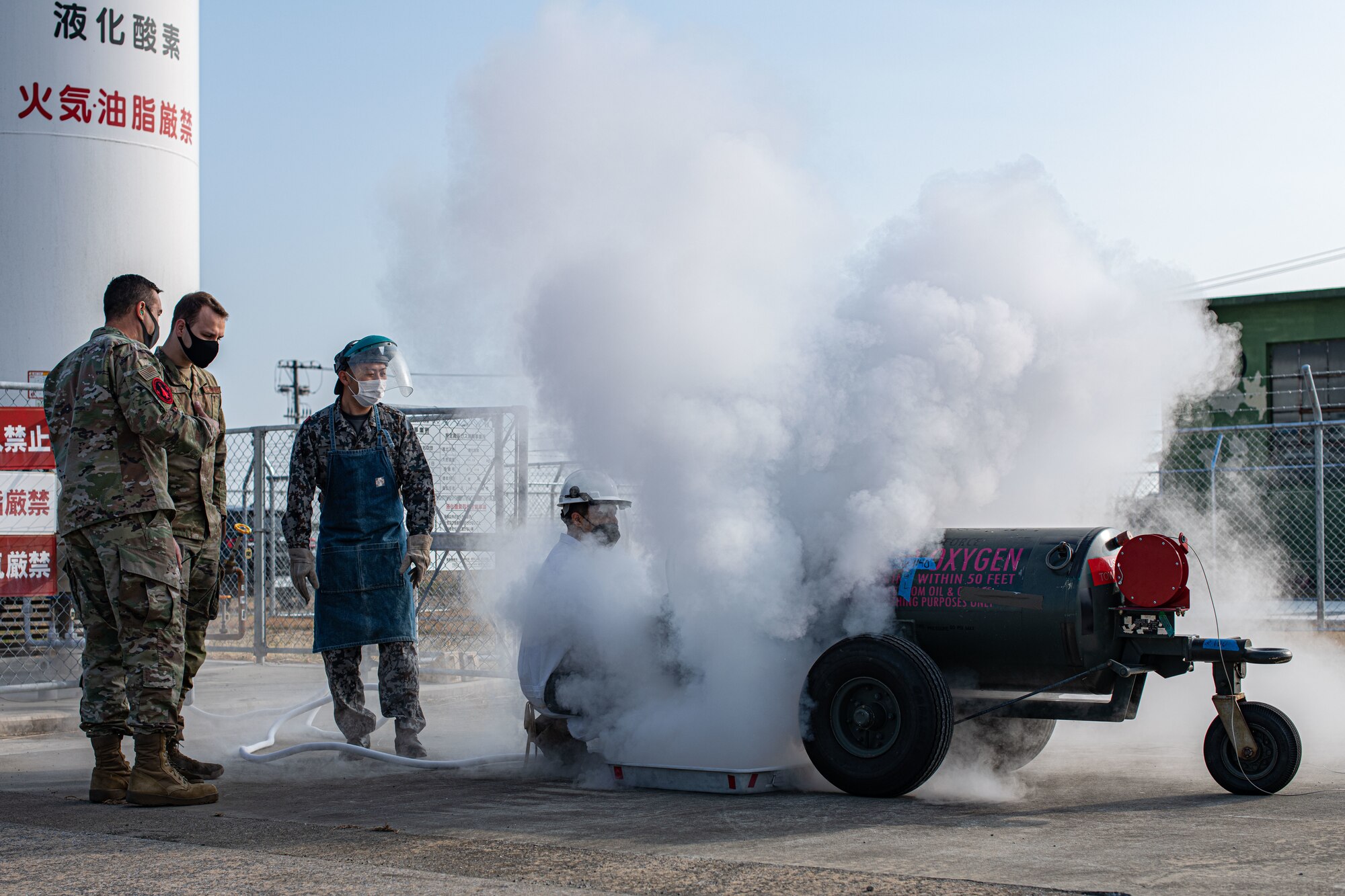 Airmen and a Japan military member fill a liquid oxygen tank.