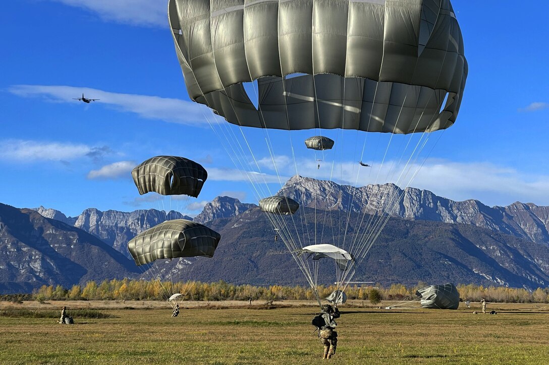 Army paratroopers land on flat ground, with mountains in the background.
