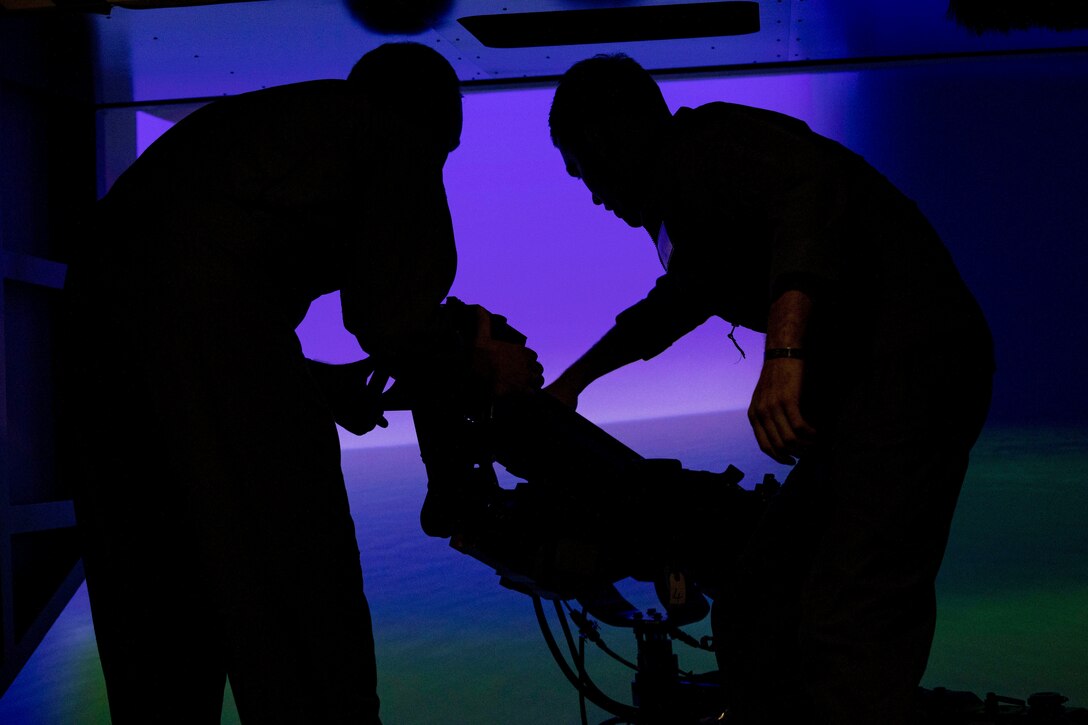 Two Marines stand next to a device in a room illuminated by purple light.