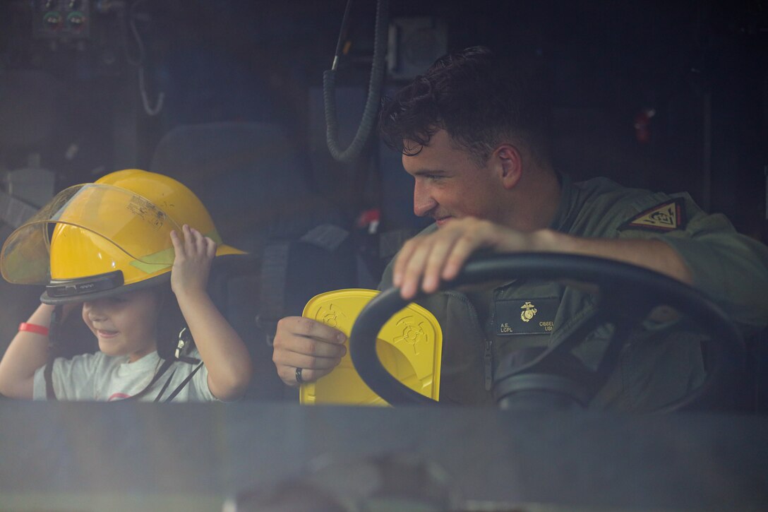 U.S. Marine Corps Lance Cpl. Austin Cissell, Aircraft Rescue and Firefighting, Marine Corps Air Station Kaneohe Bay, shares his helmet with a child during a National Night Out event, Marine Corps Base Hawaii,, Nov. 16, 2022. The event is an annual community-building campaign that promotes police-community partnerships and neighborhood camaraderie to enhance the relationship between neighbors and law enforcement while bringing back a true sense of community. (U.S. Marine Corps Photo by Gunnery Sgt. Orlando Perez)