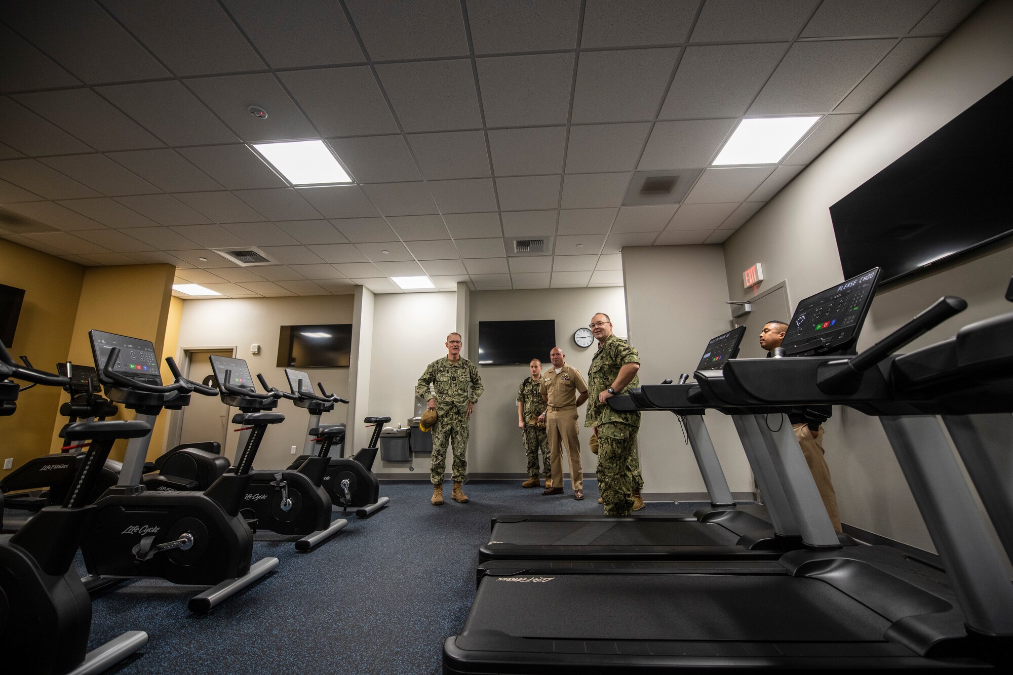 Navy personnel stand around a new gym room.