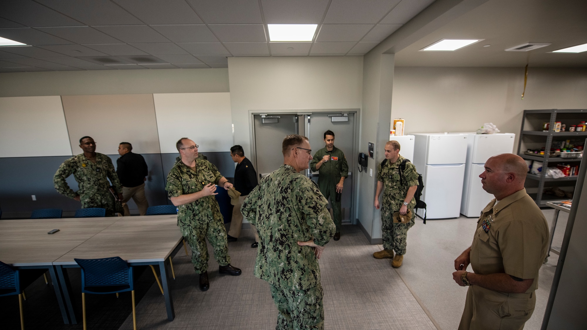 Navy personnel stand around in a kitchen.