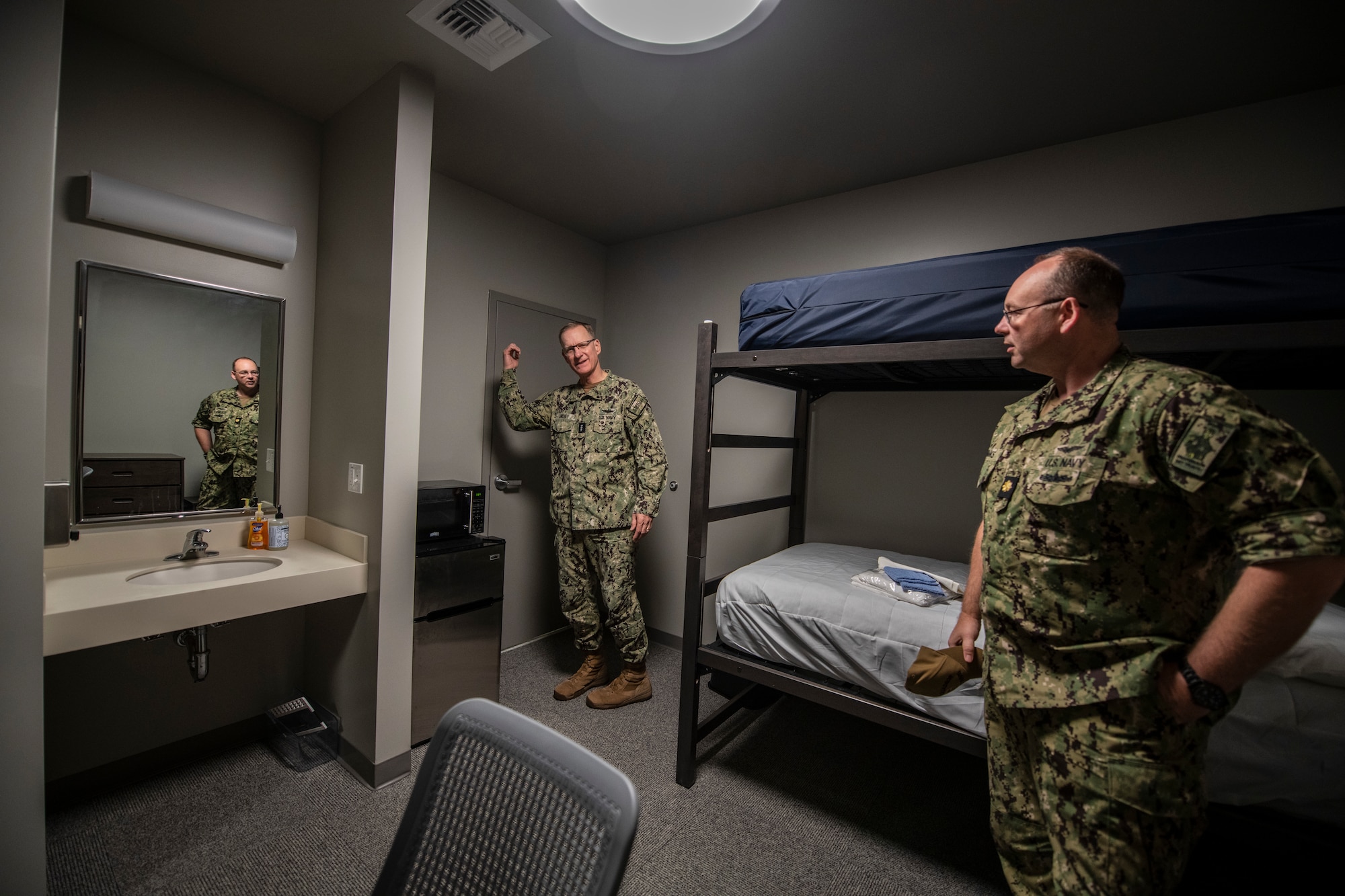 Navy personnel stand around an empty dorm room.