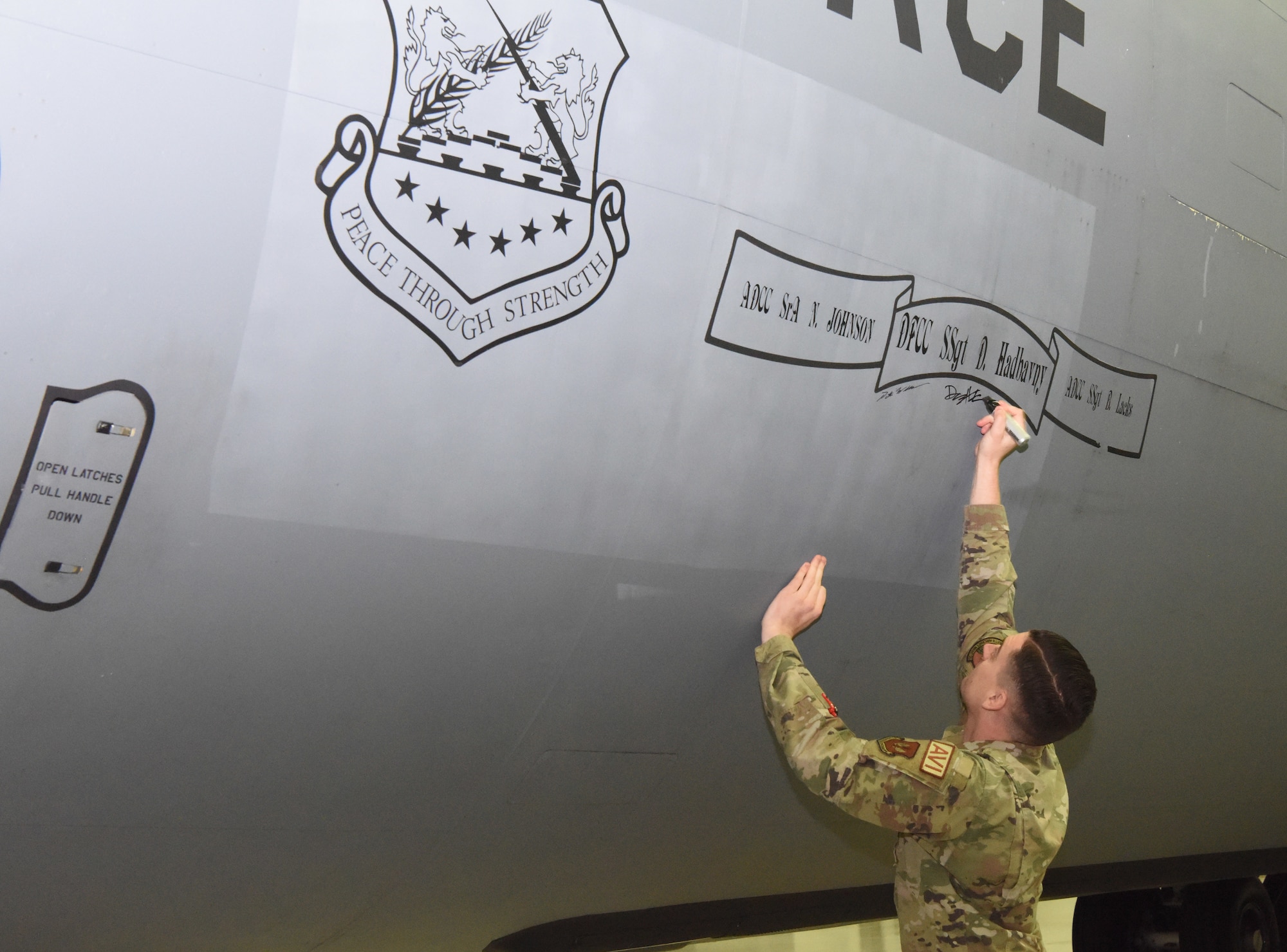 U.S. Air Force Staff Sgt. Damon Hadbavny, 100th Aircraft Maintenance Squadron dedicated flying crew chief for KC-135 Stratotanker 7999, signs under his name, displayed on the body of the jet, after a retirement ceremony for the aircraft Nov. 23, 2022, at Royal Air Force Mildenhall, England.  This was the first official retirement of a KC-135 at RAF Mildenhall. The 59-year-old tanker, which bears the World War II legacy nose art “Wolff Pack,” has taken its last flight and is now at its final resting place in “The Bone Yard” at Davis-Monthan Air Force Base, Arizona. (U.S. Air Force photo by Karen Abeyasekere)