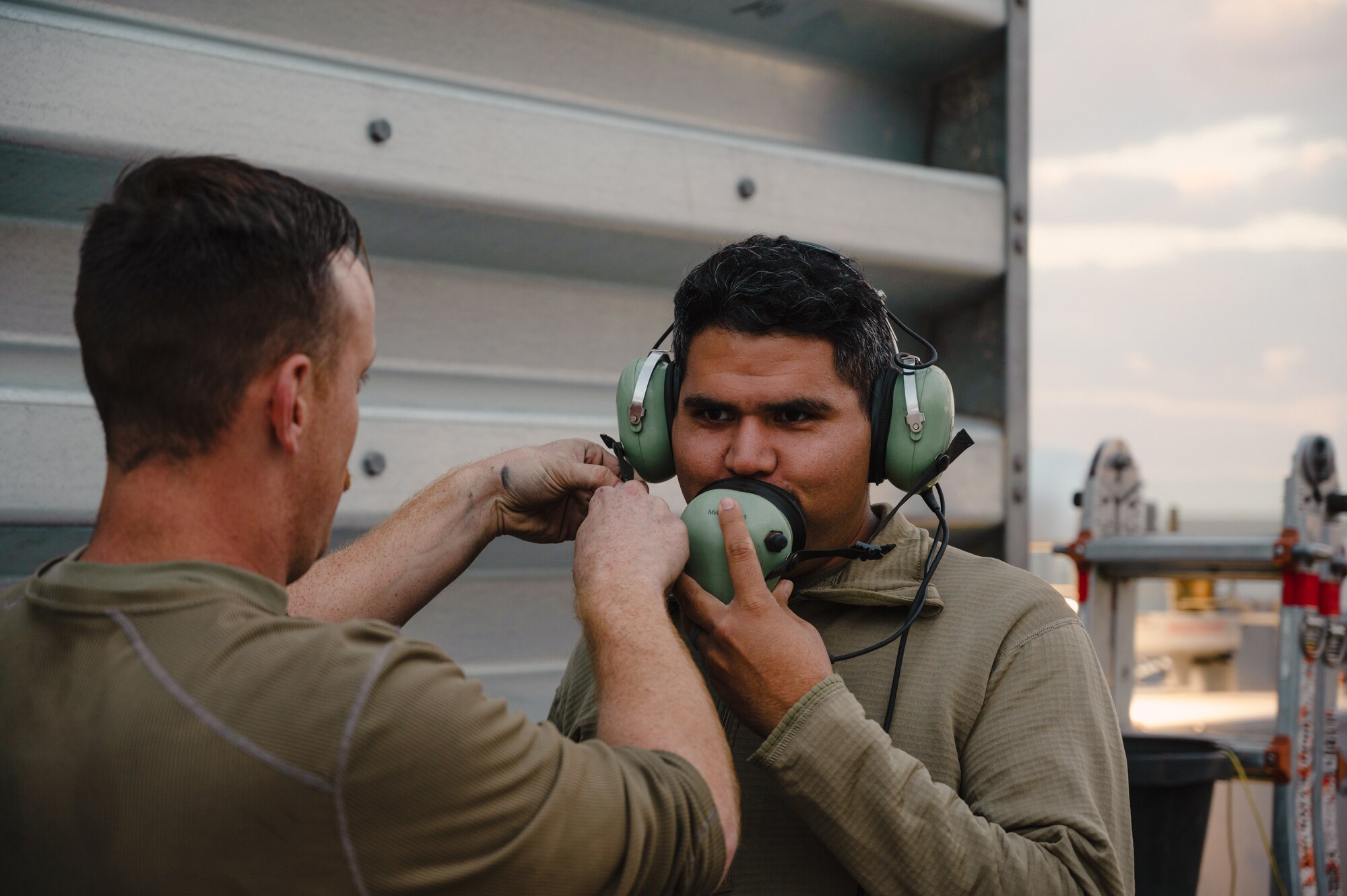 Senior Airman Dennis M. Hatcher, a crew chief with the 389th Expeditionary Fighter Squadron, adjusts a communication device on Senior Airman Hector J. Gomez, Jr., 332d Expeditionary Logistics Readiness Squadron Fuels Management Flight as part of the “Maintainer for a Day” program at an undisclosed location, Nov. 10, 2022. Maintainer for a Day is an initiative that pairs Airmen across a variety of career fields with members of aircraft maintenance shops for a hands-on learning experience with F-15E Strike Eagle fighter jets. (U.S. Air Force photo by Tech. Sgt. Richard Mekkri)