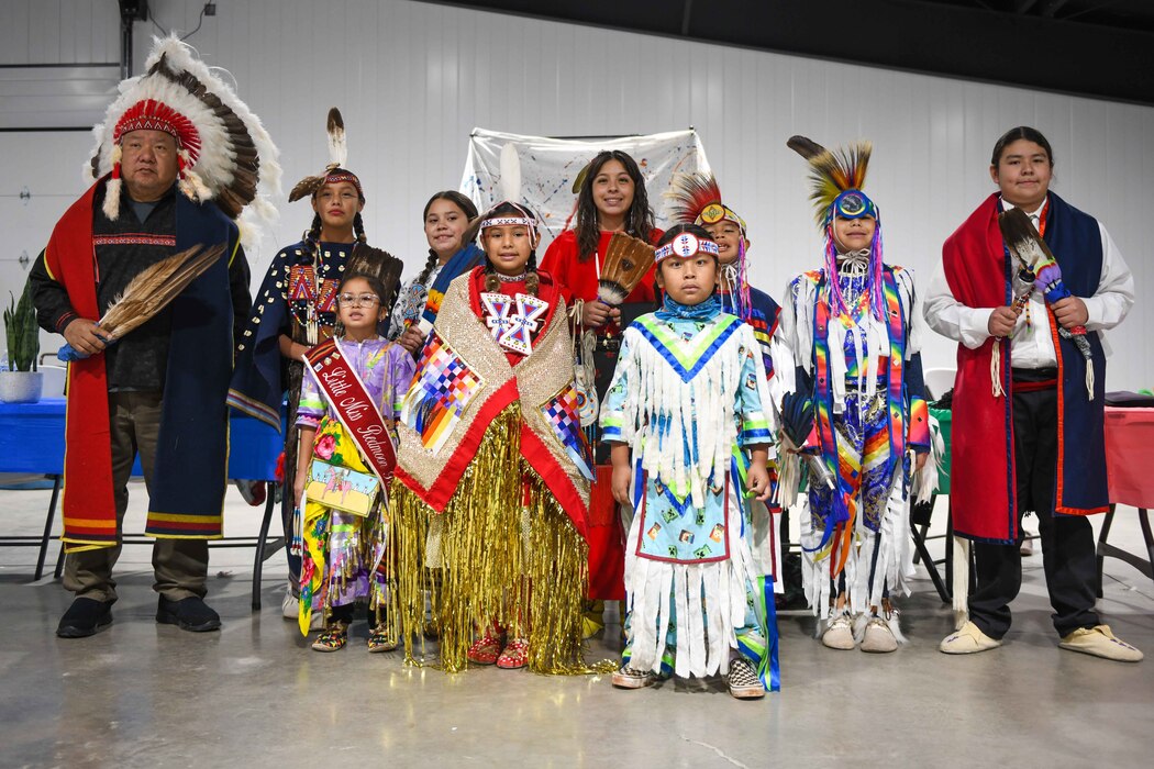 Comanche Nation Youth Dancers pose for a photo with Chief Jason Goodblanket, left, of the Cheyenne Tribe at the Jackson County Expo Center on Nov. 19, 2022, in Altus, Oklahoma. Goodblanket commemorated the event before the dancers took center stage. (U.S. Air Force photo by Airman 1st Class Kari Degraffenreed)