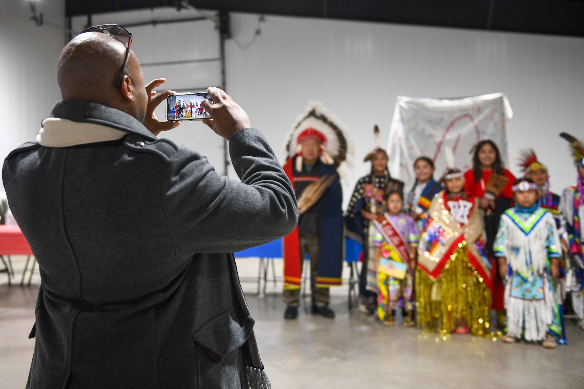Col. Patrick Brady-Lee, 97th Air Mobility Wing vice commander snaps a picture of the Comanche Nation Youth Dancers along with Chief Jason Goodblanket of the Cheyenne Tribe at the Jackson County Expo Center Nov. 19, 2022, in Altus, Oklahoma. Brady-Lee, base personnel, and other Altus community members were asked to jump in with the dancers near the end of the performance. (U.S. Air Force photo by Airman 1st Class Kari Degraffenreed)